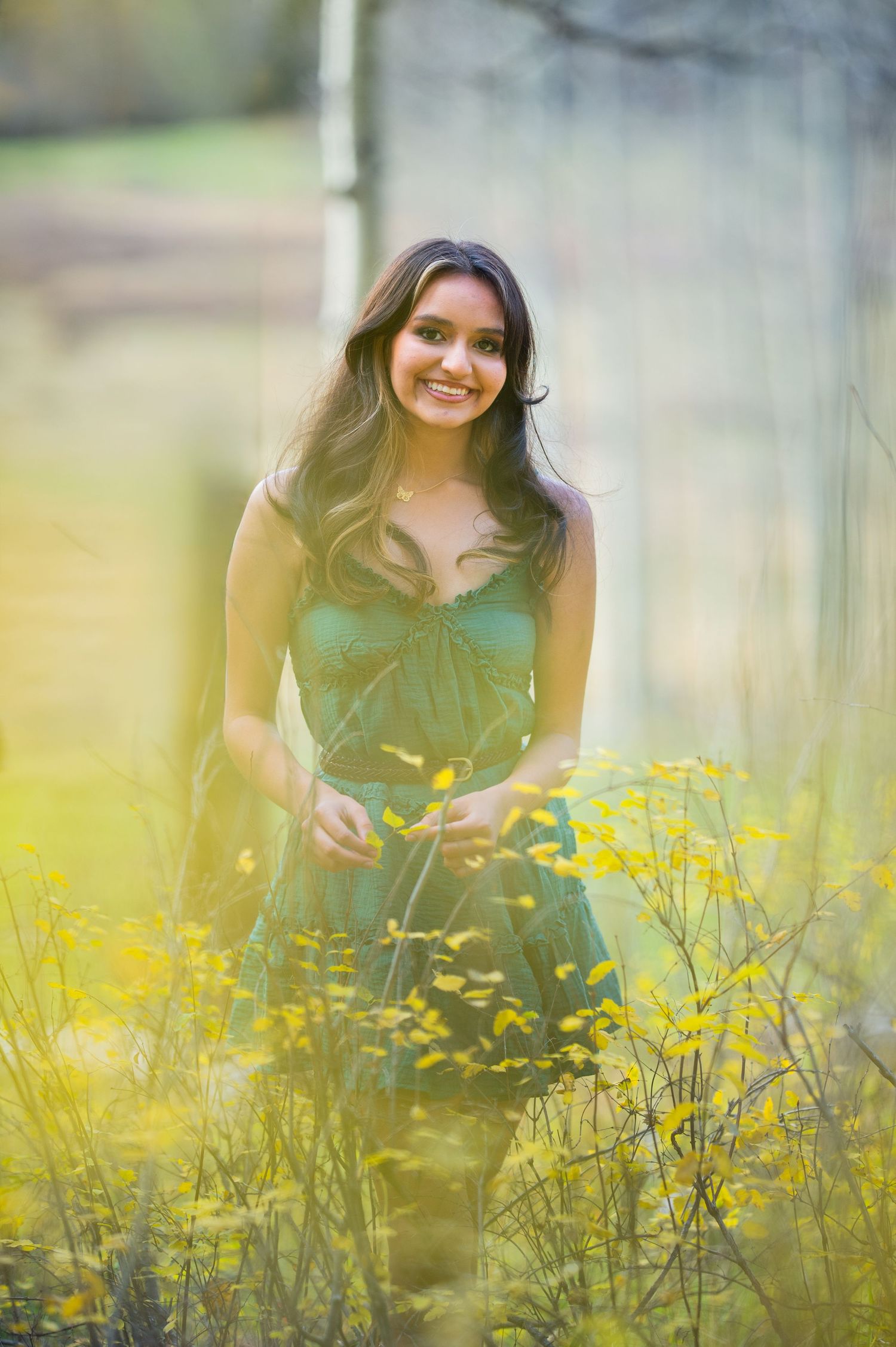 Person in a green dress poses among vibrant yellow wildflowers in a dreamy outdoor nature setting.