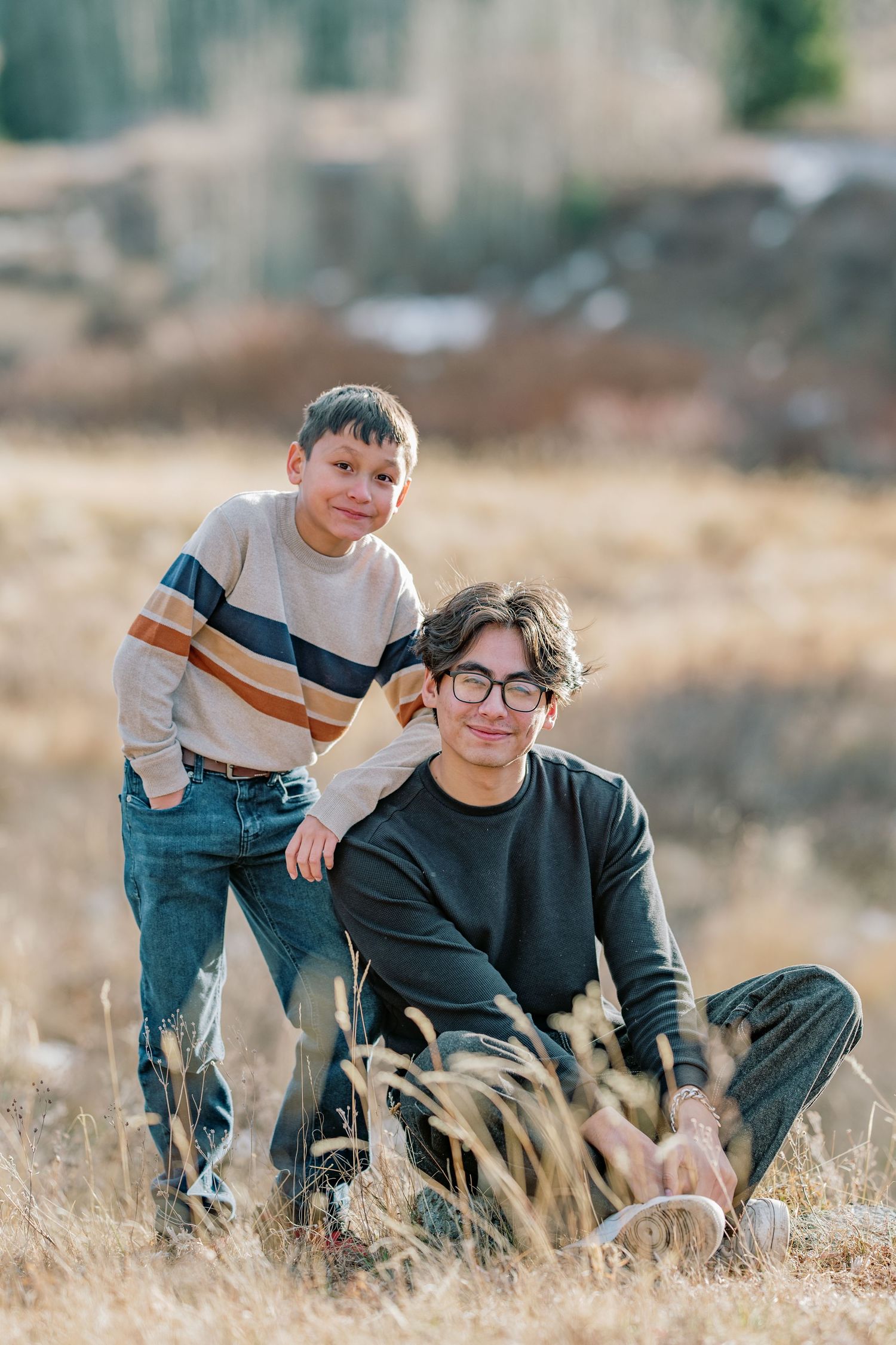 Two people share playful moments in a sunlit field of tall grass during an outdoor photo session.