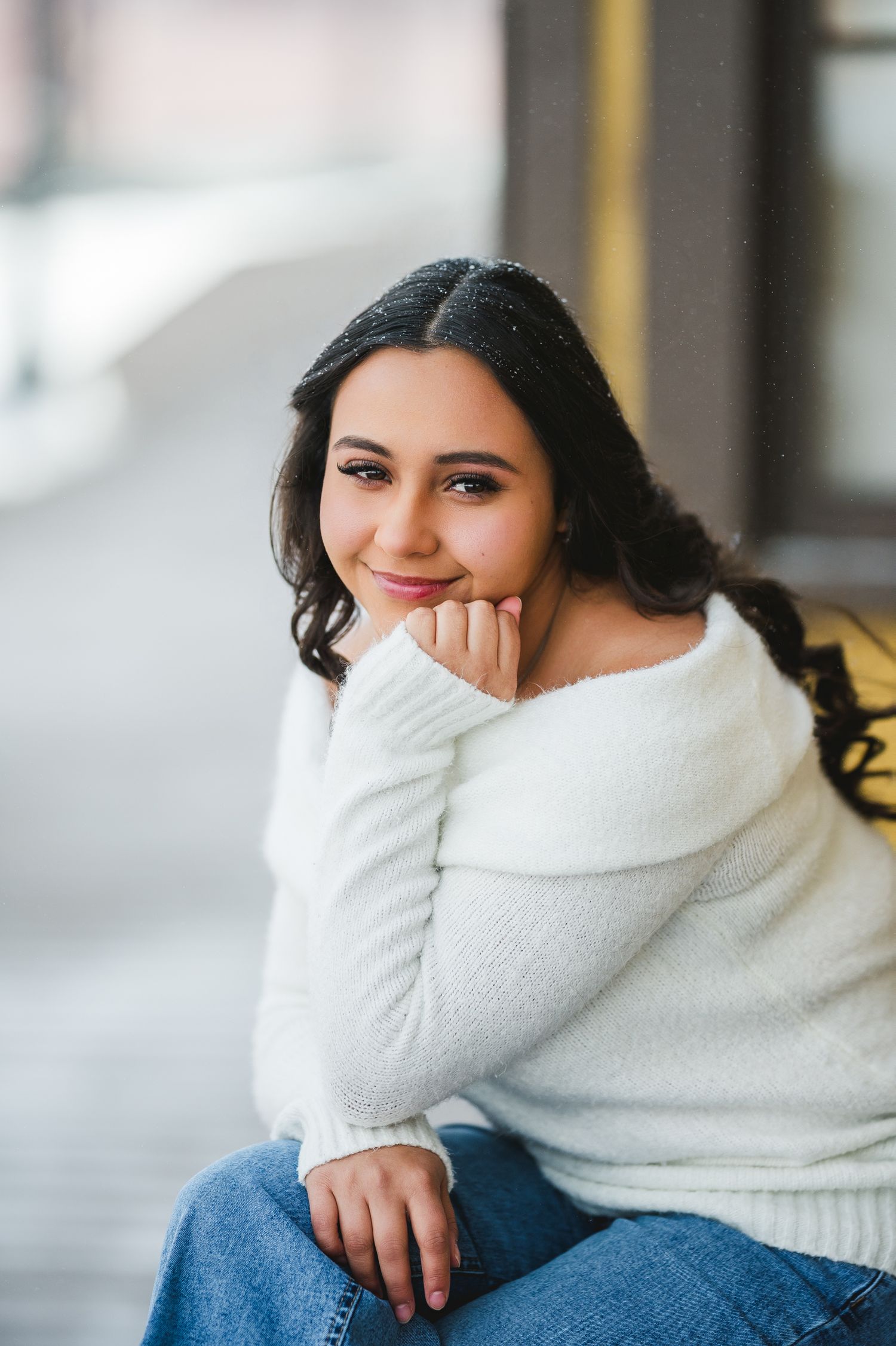 Person wearing cozy white turtleneck sweater smiles while sitting on blue couch in natural window light.