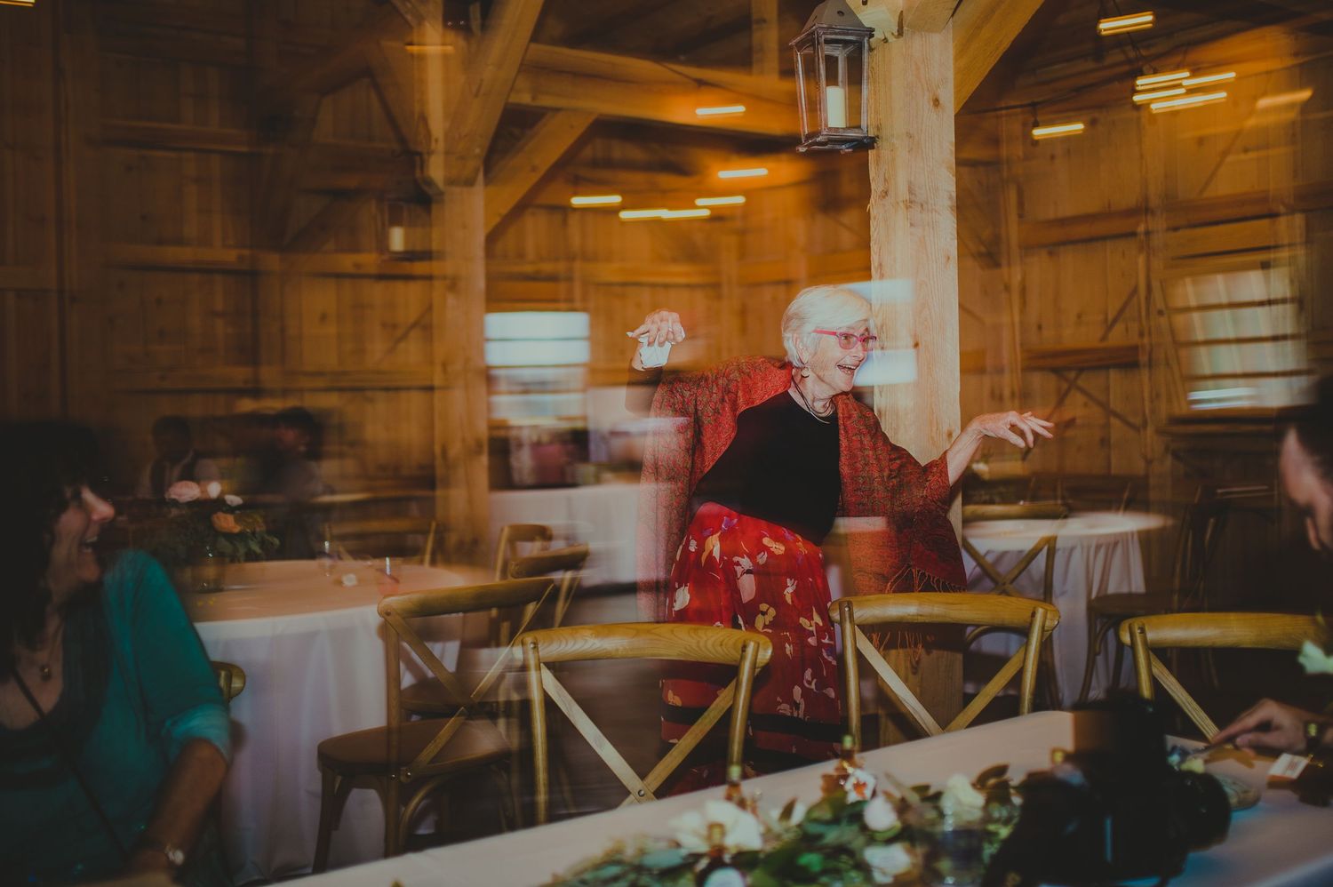 Person in festive red attire gesturing animatedly during a celebration in a warmly lit wooden venue.