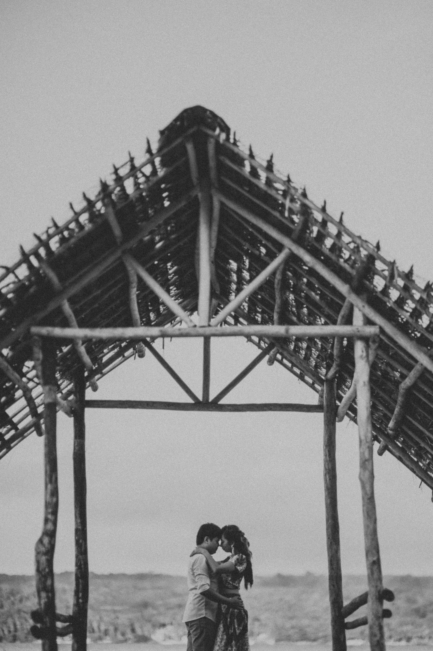 A romantic scene under a traditional thatched roof structure in black and white.