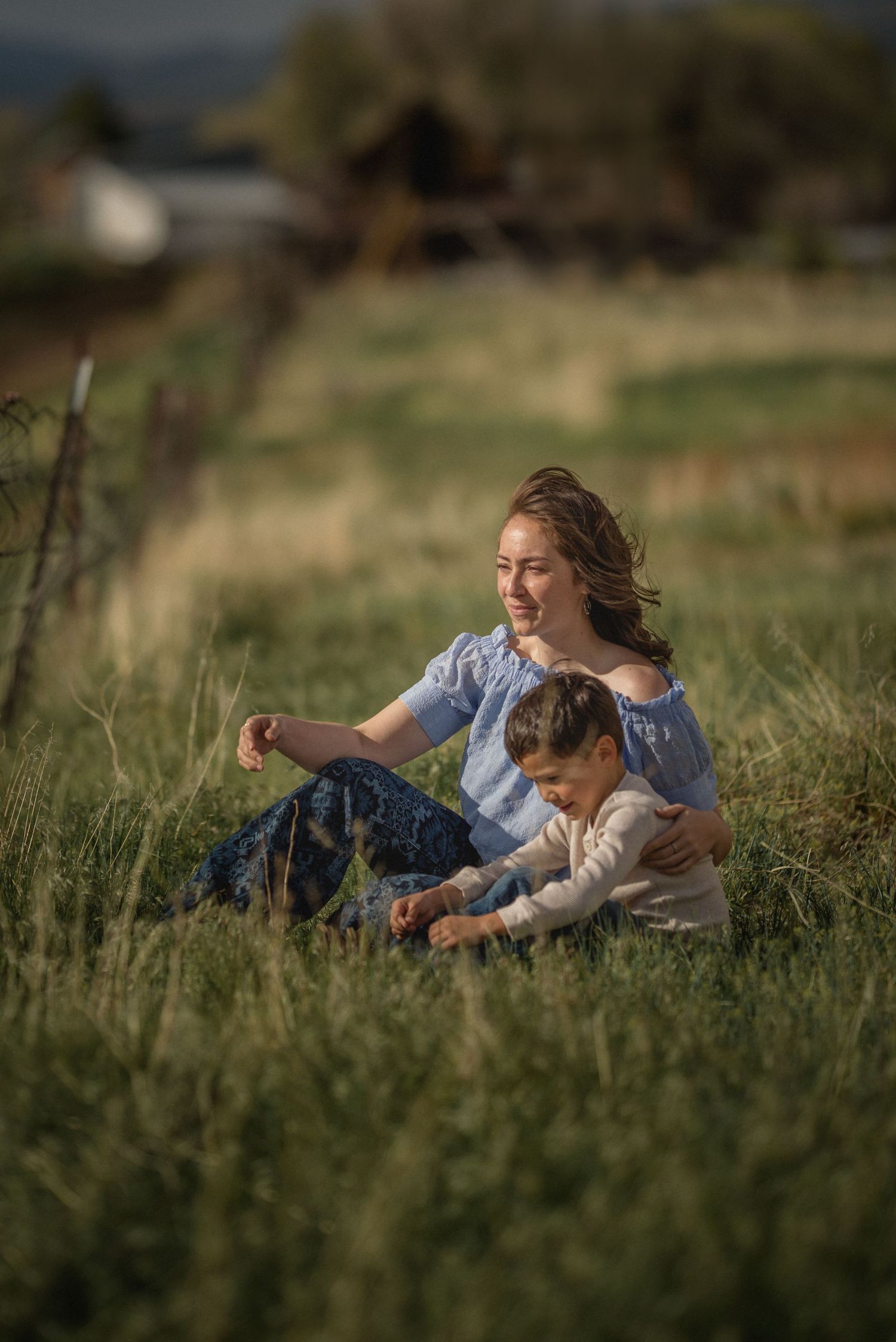 A tender moment shared between two people sitting in a sunlit meadow with tall grass and golden evening light.