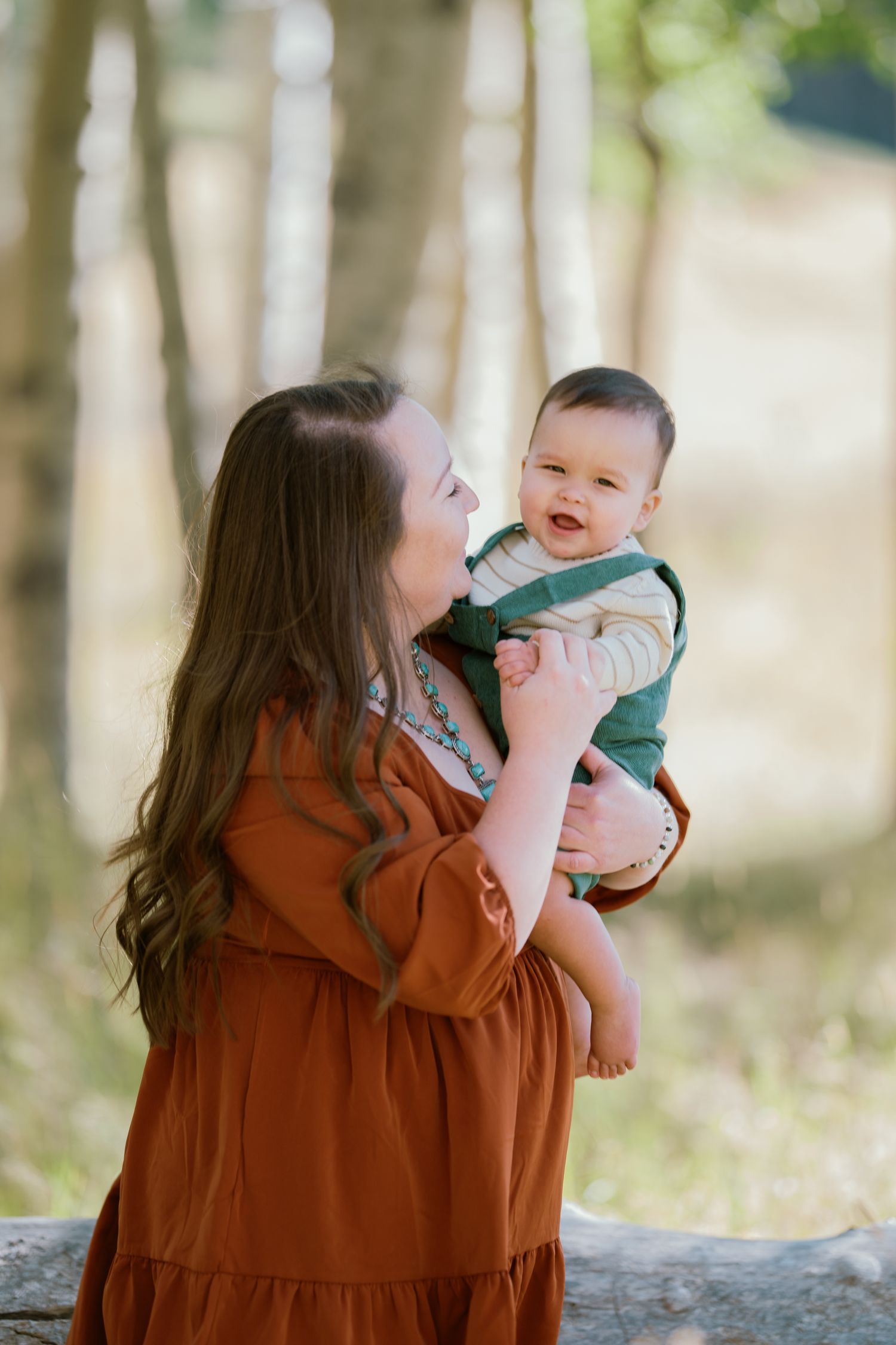 A tender moment between parent and baby in a rustic outdoor setting with trees in the background.