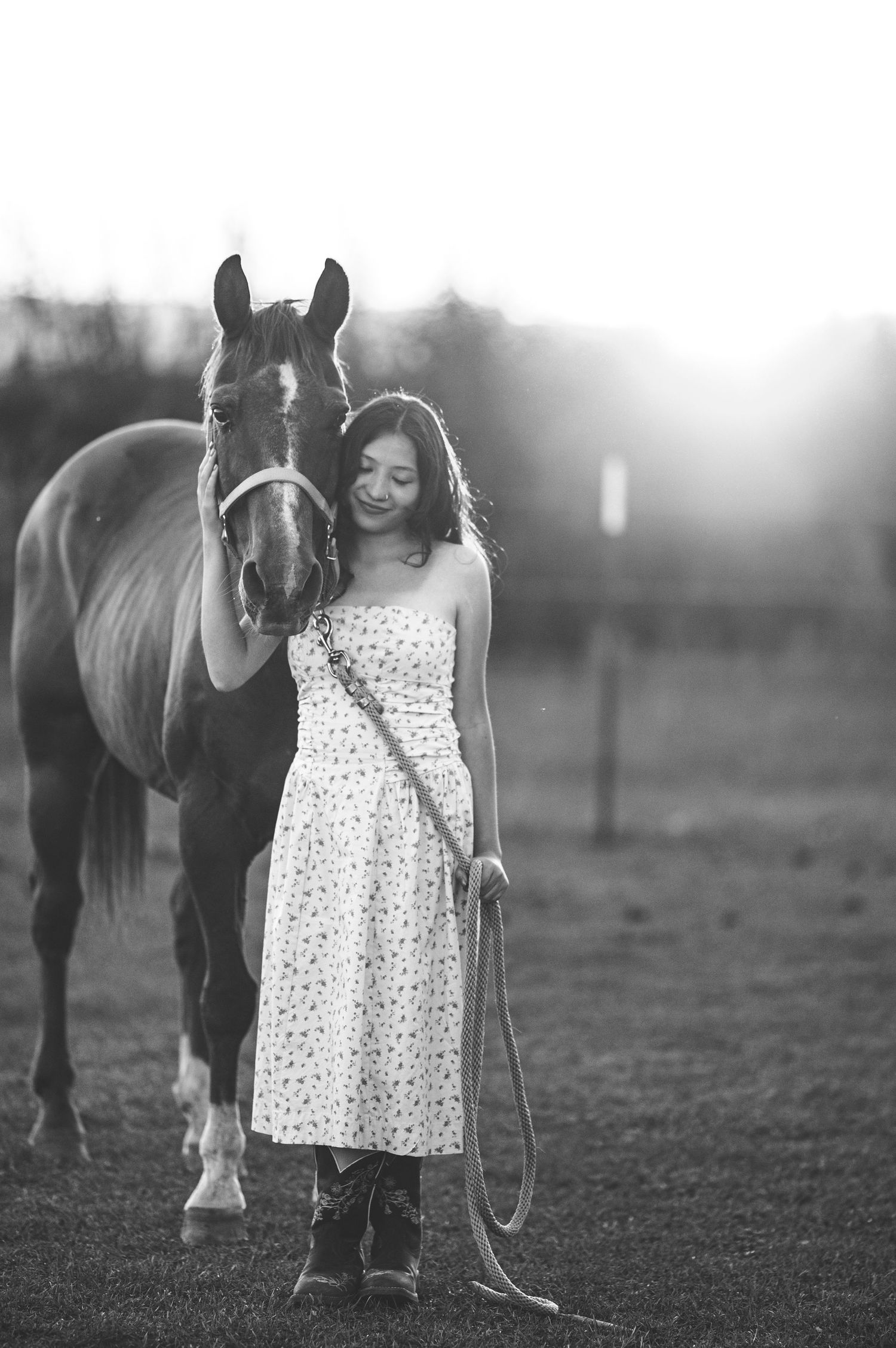 A person in a white polka dot dress pets a dark horse in a dreamy black and white outdoor setting.