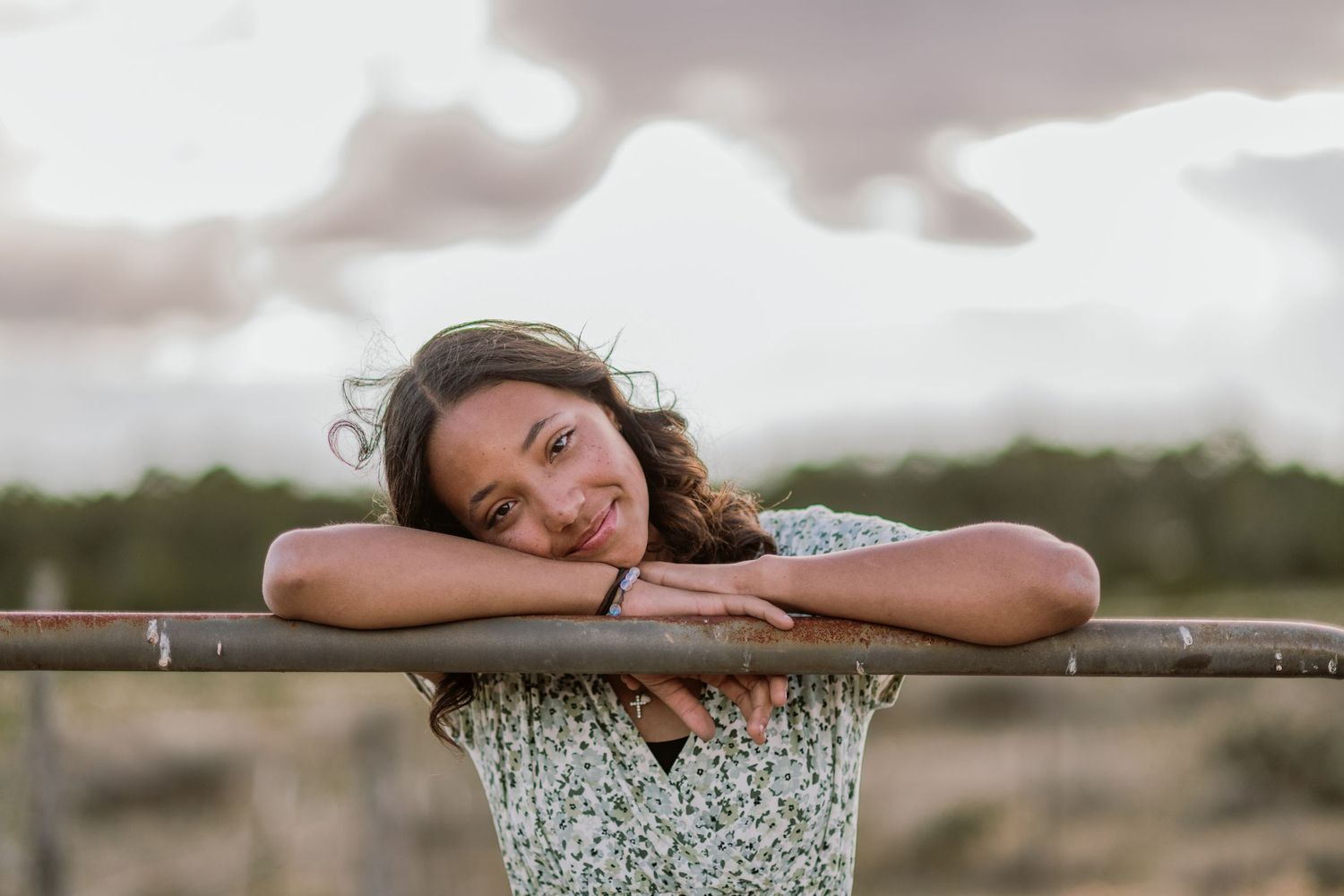 Person resting peacefully on a rustic wooden fence with a dreamy countryside backdrop at sunset.