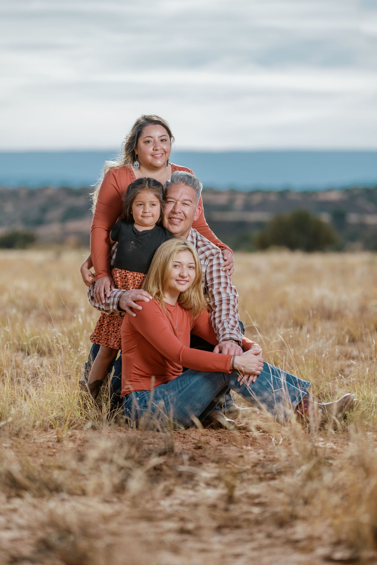 Family portrait session in tall golden grass field during sunset with warm candid interactions.