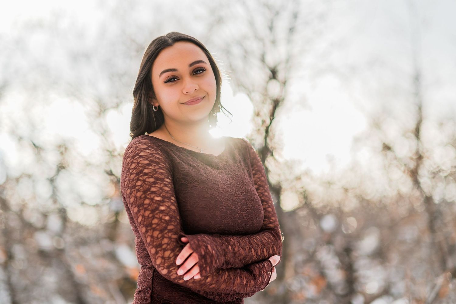 A person wearing a brown knit sweater poses outdoors during winter with soft bokeh lighting.