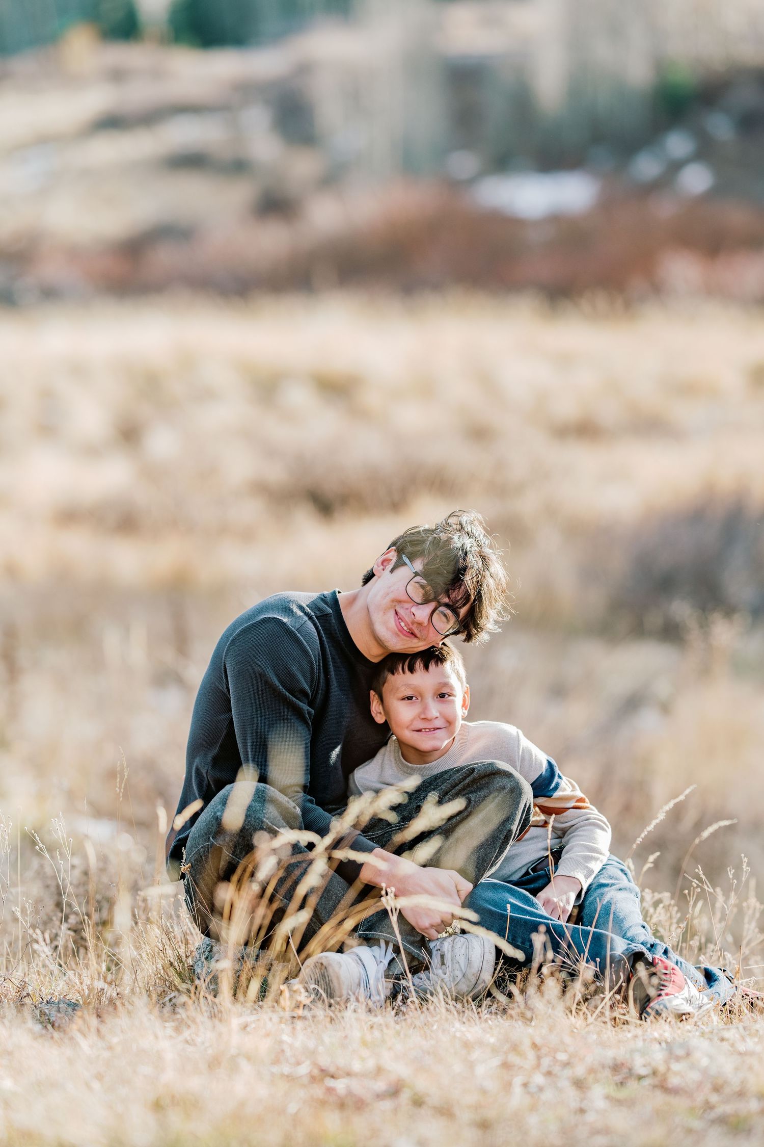 Two people sitting close together in a golden autumn field during sunset with soft natural lighting.