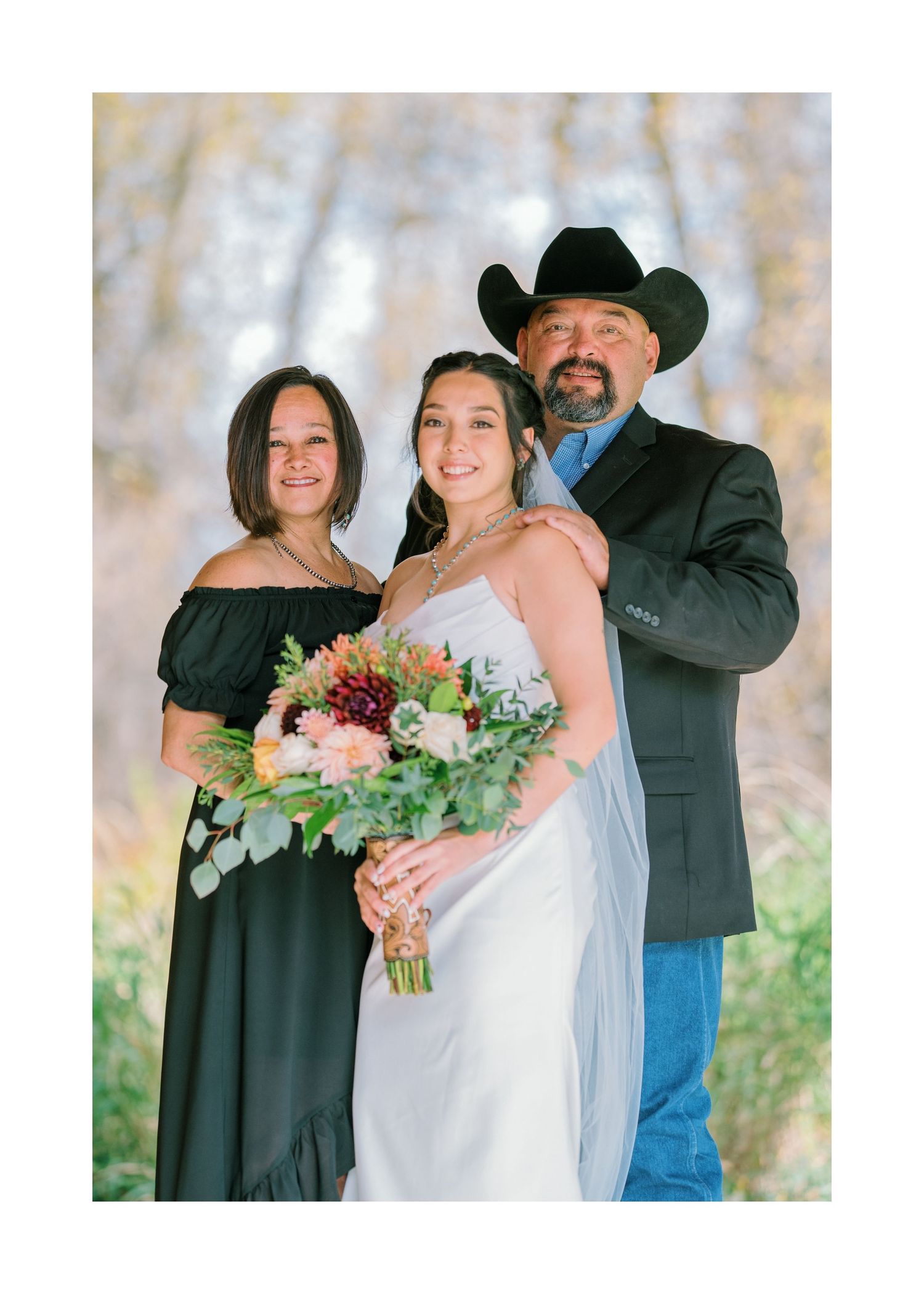 A serene outdoor winter wedding scene with a bride in white holding a colorful floral bouquet standing with her family.