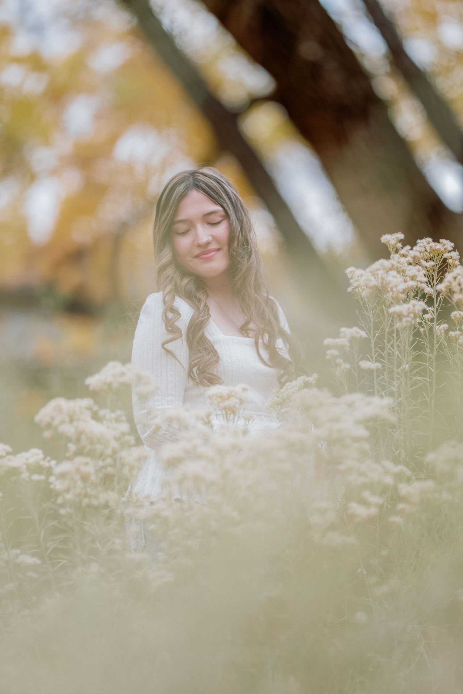 A woman in a white dress stands peacefully among delicate wildflowers on a dreamy autumn day.