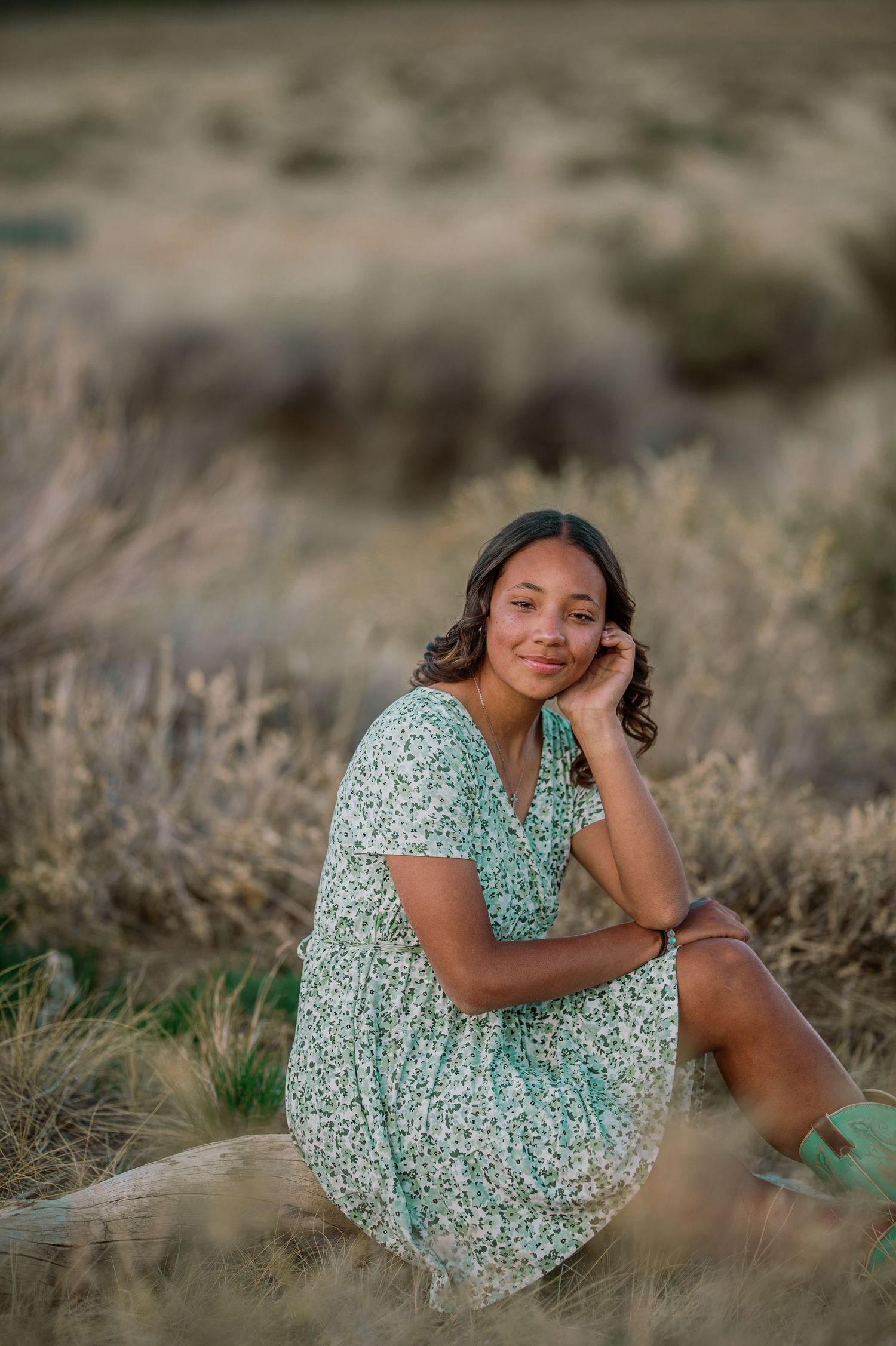 A candid outdoor portrait in a floral mint green dress sitting in dried grass fields at golden hour.
