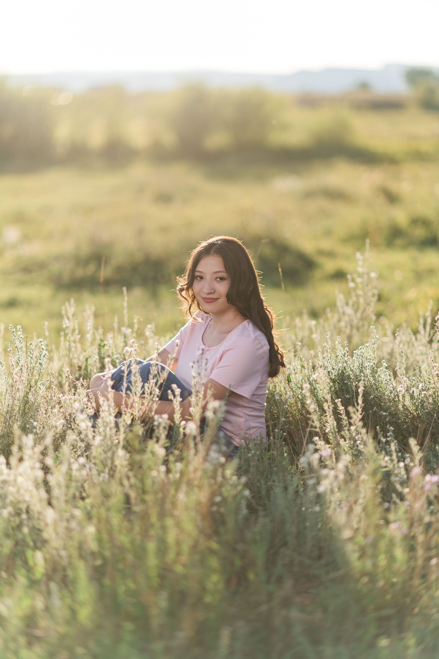 A person in pink sitting among wildflowers in a sunlit meadow during golden hour creates a dreamy outdoor portrait.