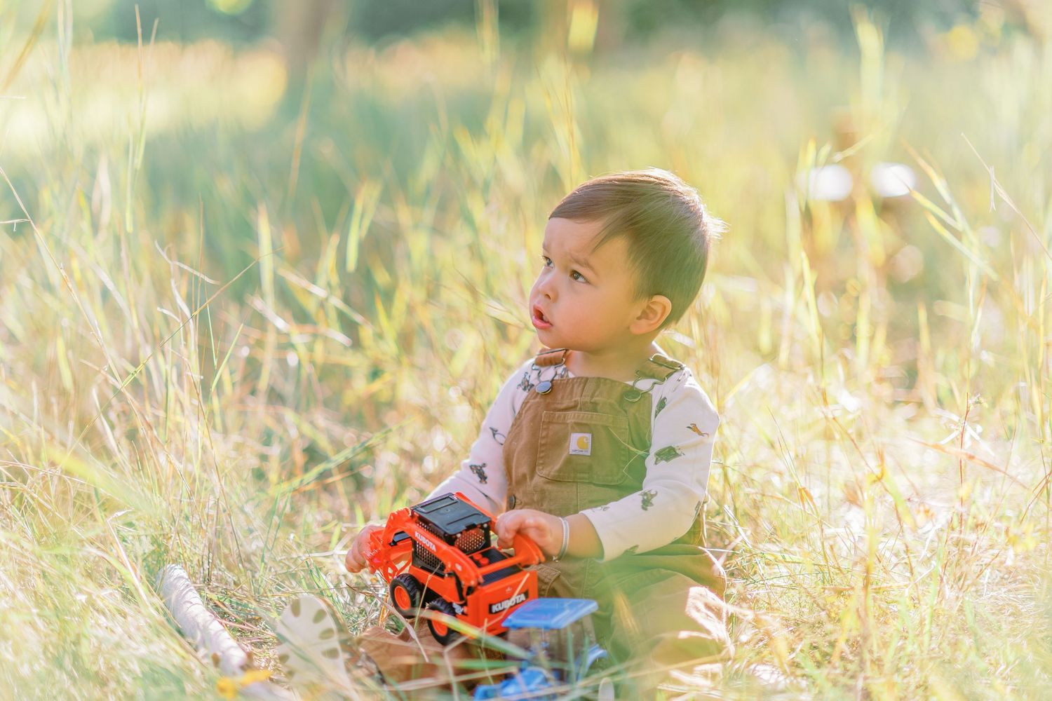 A small child sits in a grassy field on a sunny day playing with toys in a candid moment.