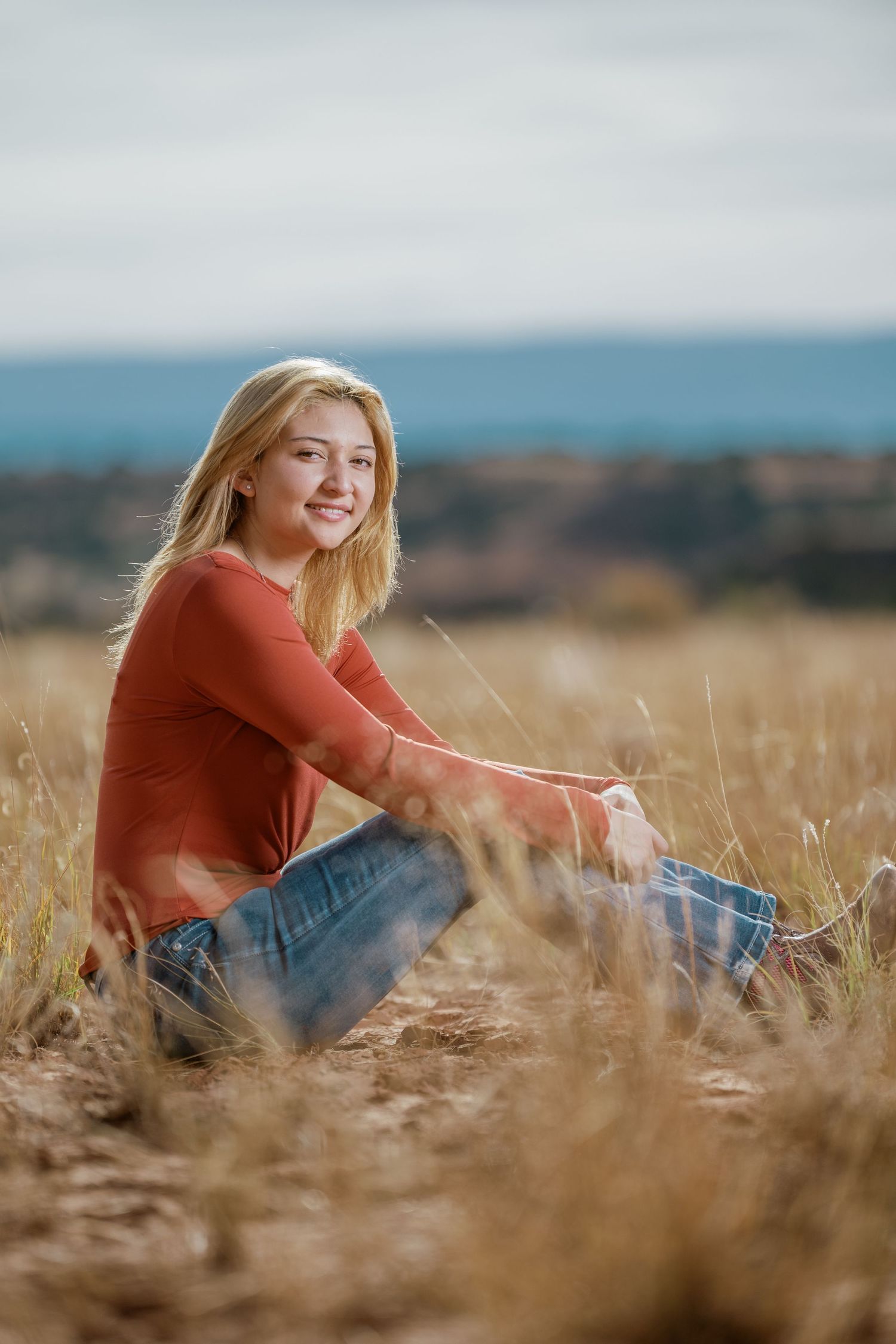 A person in a rust-colored sweater sits casually in a golden wheat field on an autumn afternoon.