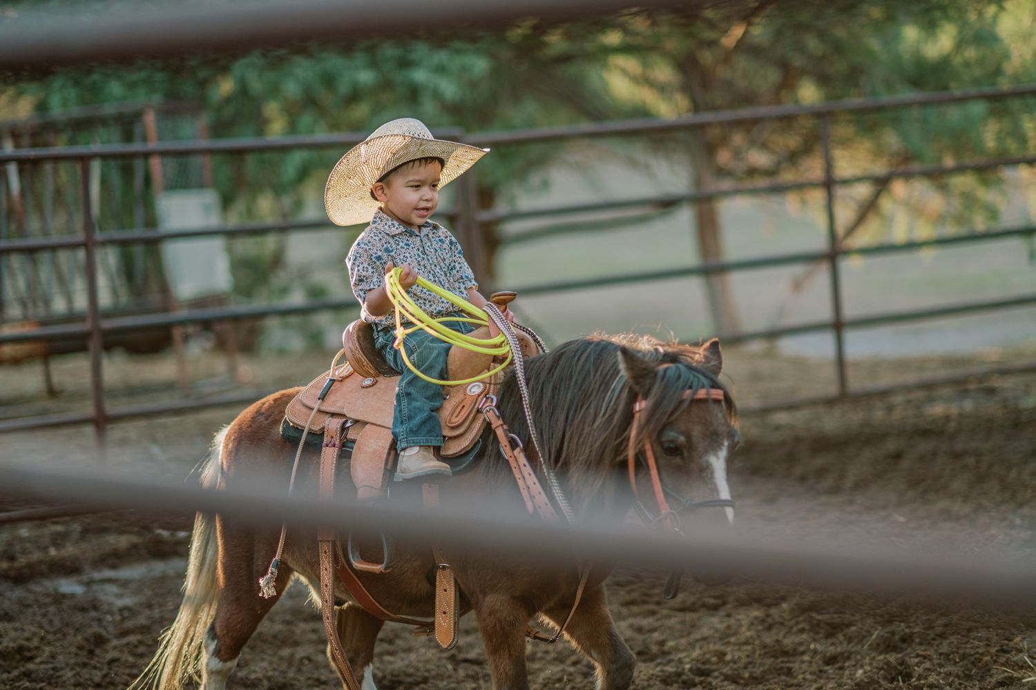 Young child in cowboy hat riding a pony while holding a lasso in a rodeo arena.