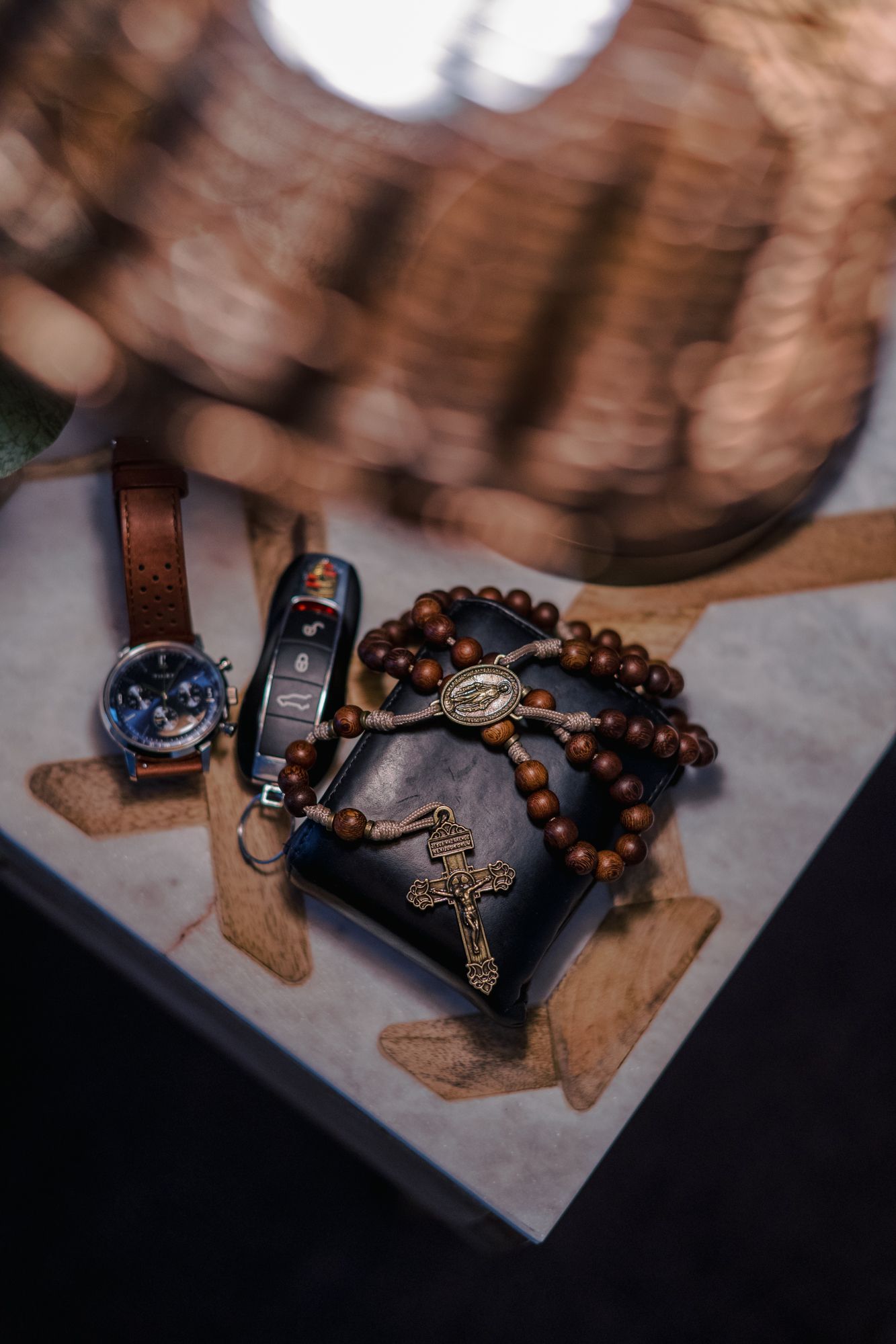 Wooden rosary beads with cross pendant and leather strap arranged on textured surface in dark moody lighting.