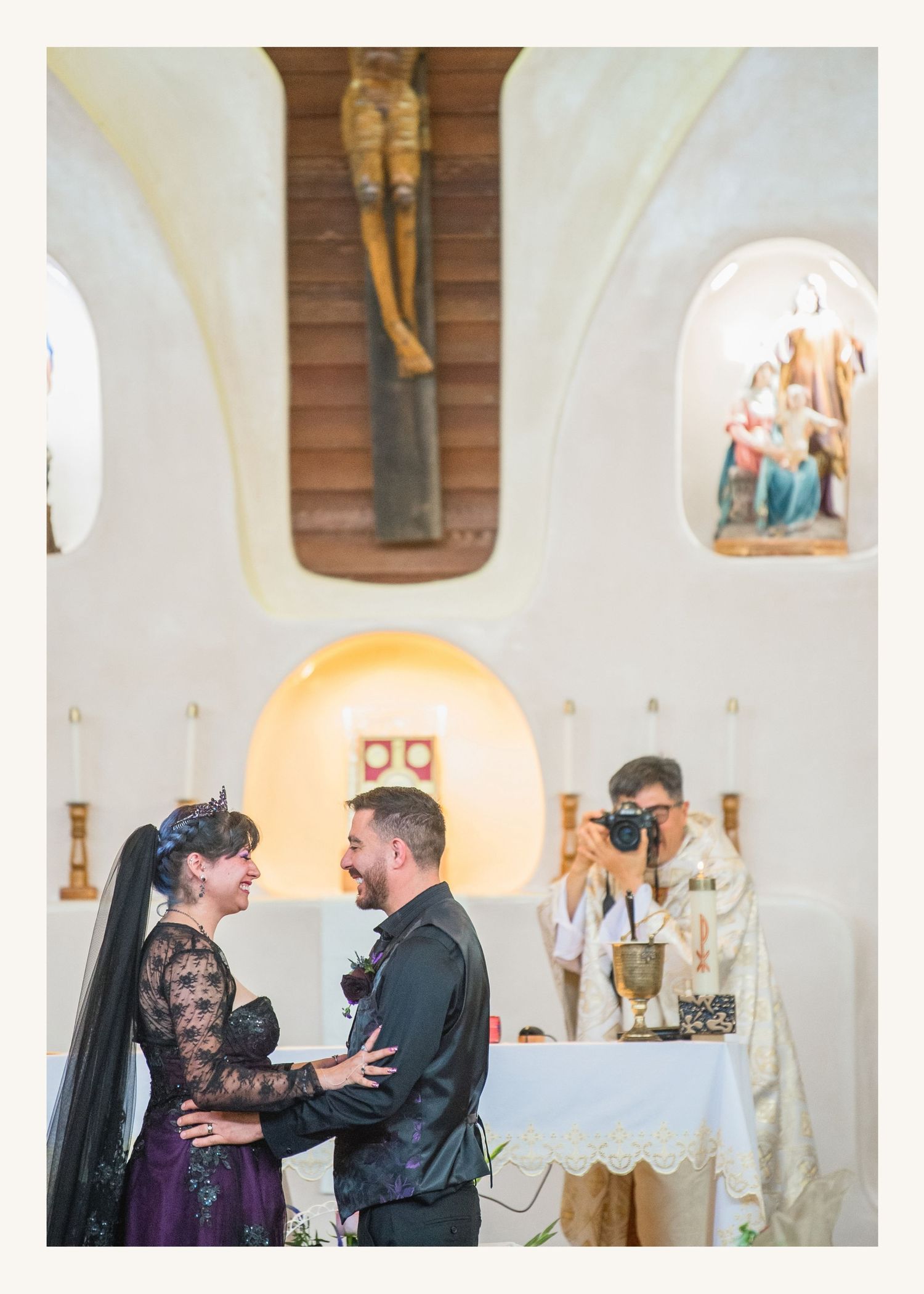 Couple shares a joyful moment during a church wedding ceremony, bride in black lace gown, groom in dark suit.