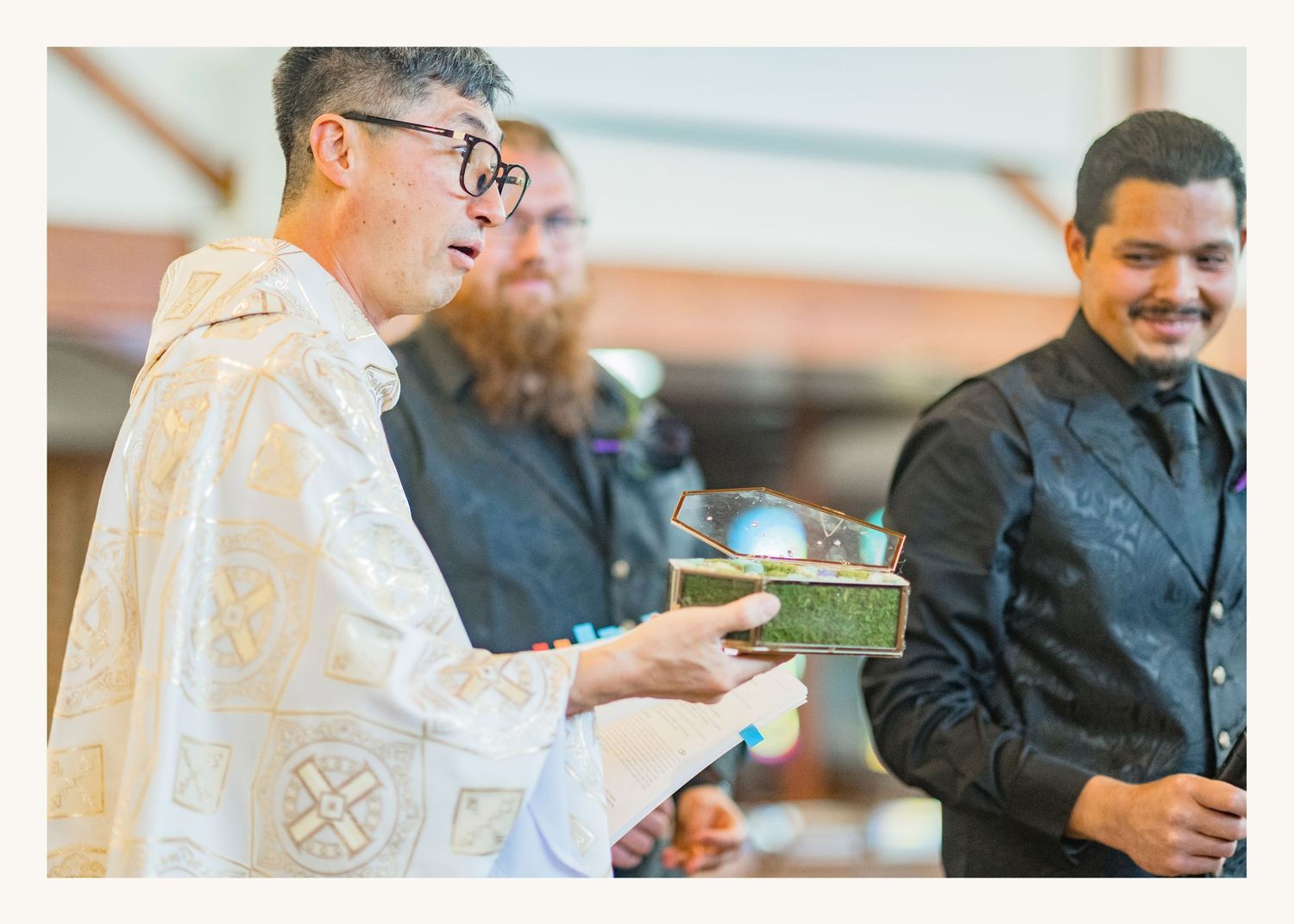 A priest in white vestments presents a ceremonial bowl during a religious ceremony with attendees in formal attire.