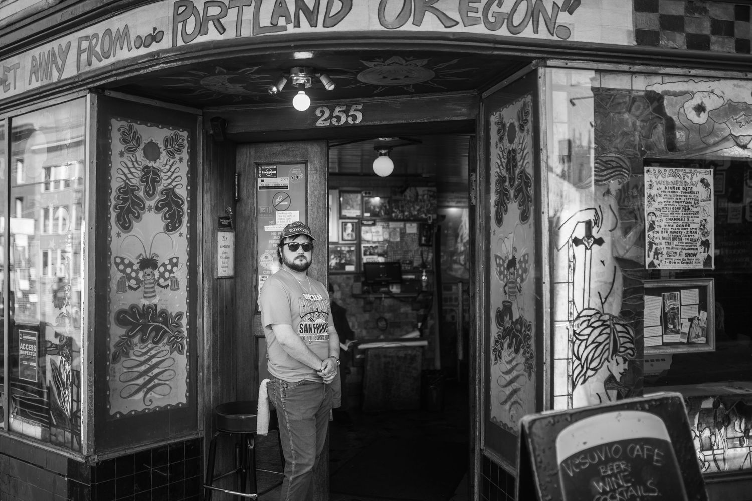 Black and white photo of a storefront entrance in Portland Oregon with eclectic decorations and posters on display.