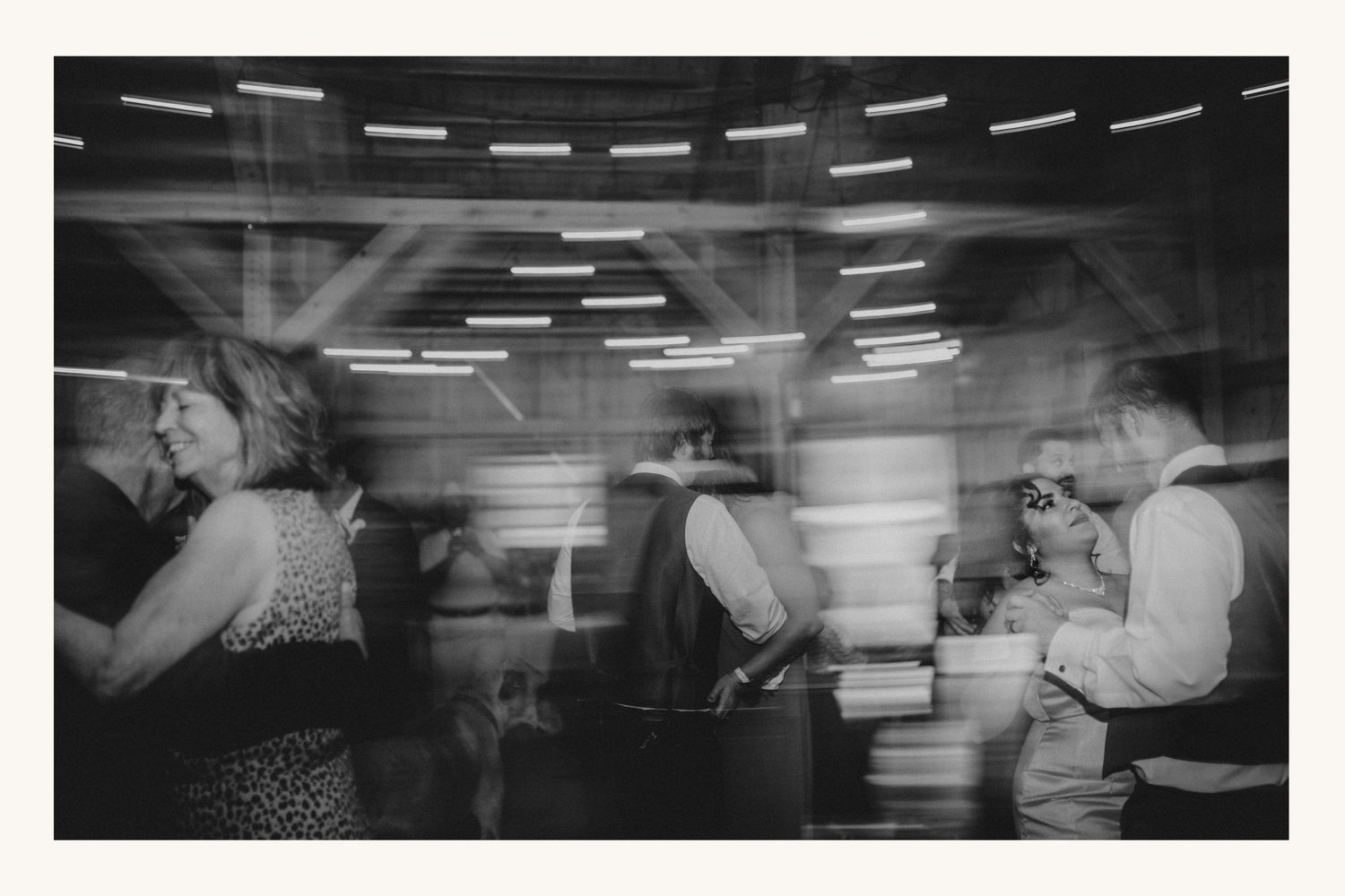 Blurry black and white photo of people dancing at a party under neon lights.