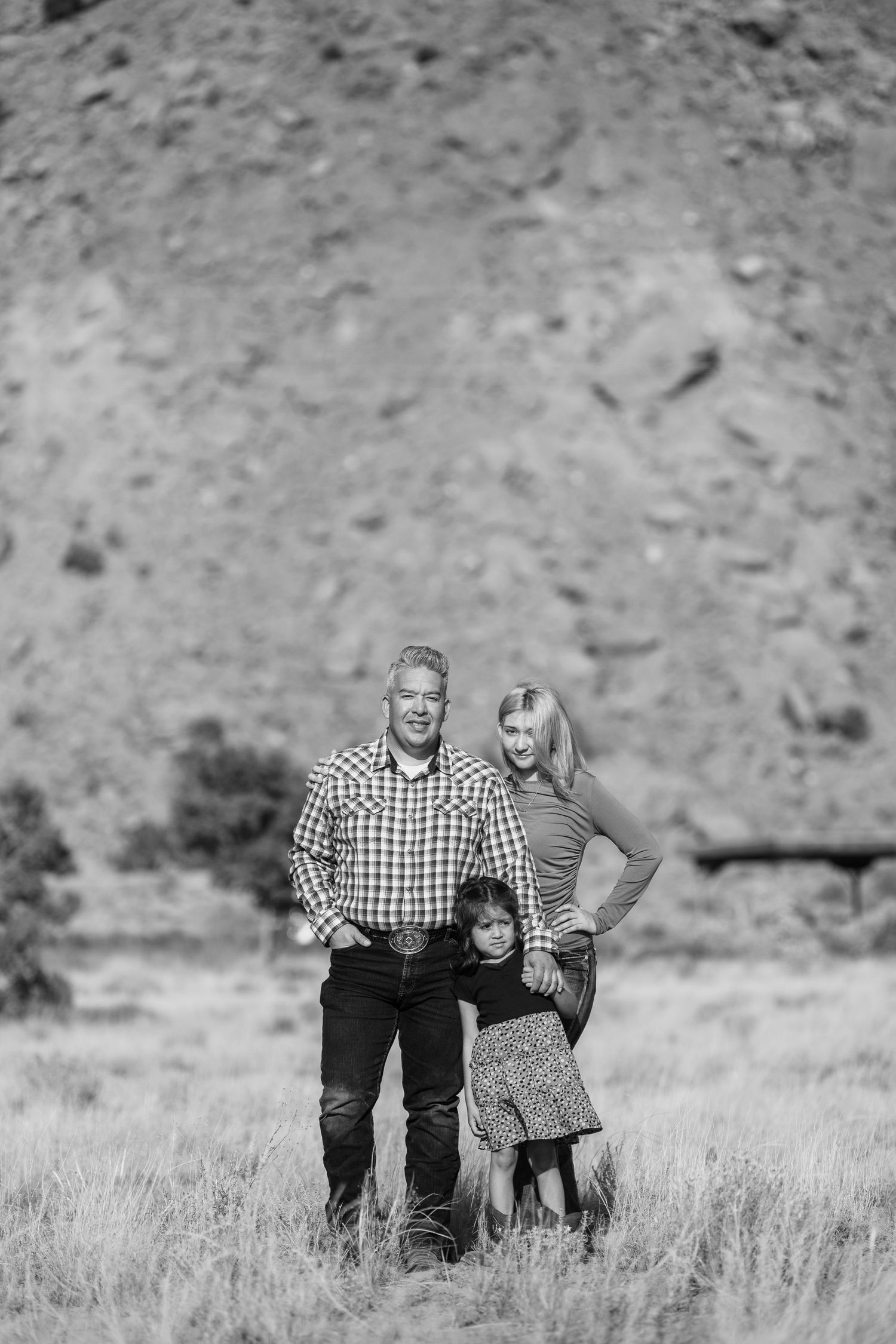 A couple standing together in a rural field with mountains visible in the background in black and white photograph.