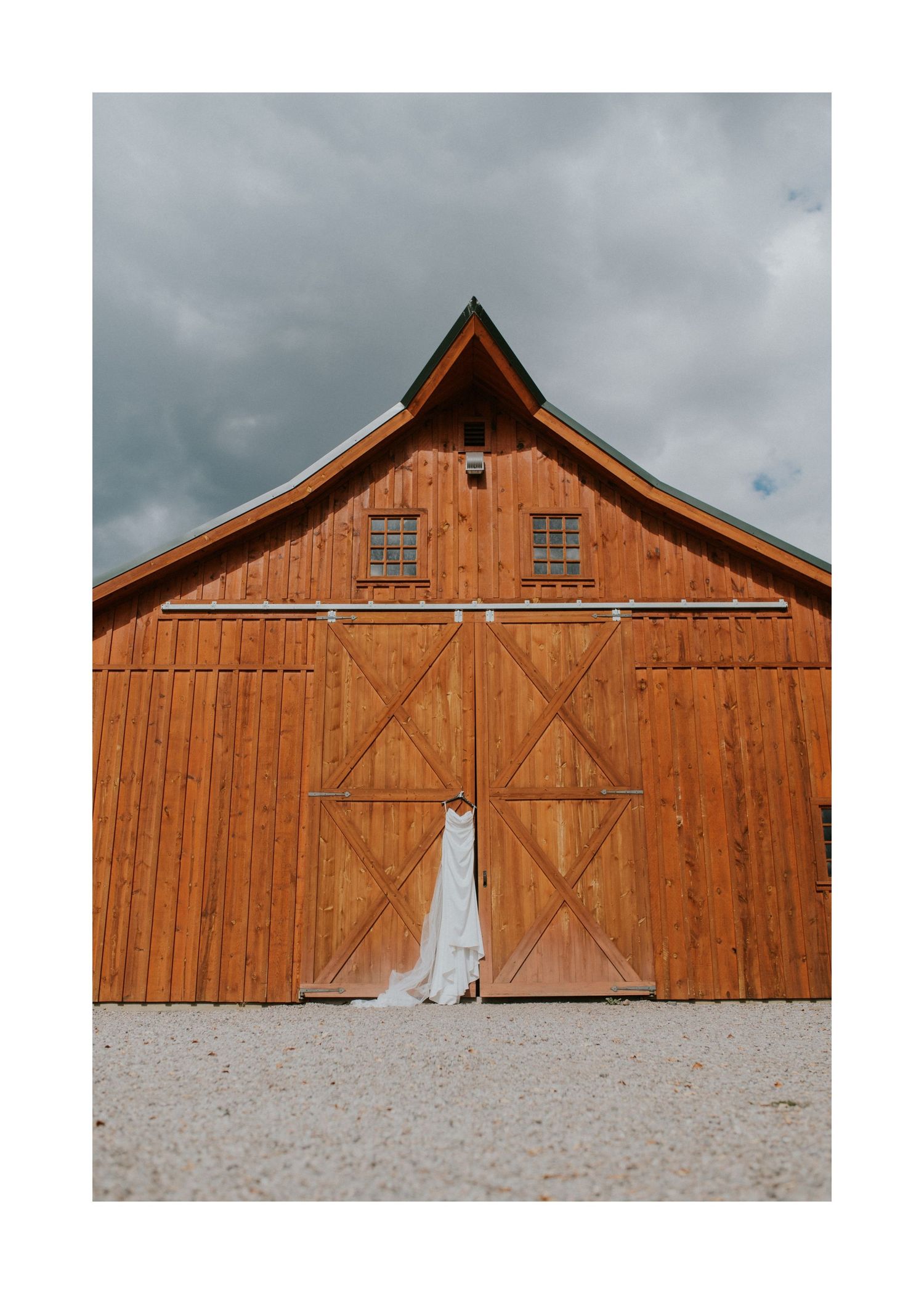 A rustic wooden barn with white trim creates a striking backdrop against a cloudy sky.