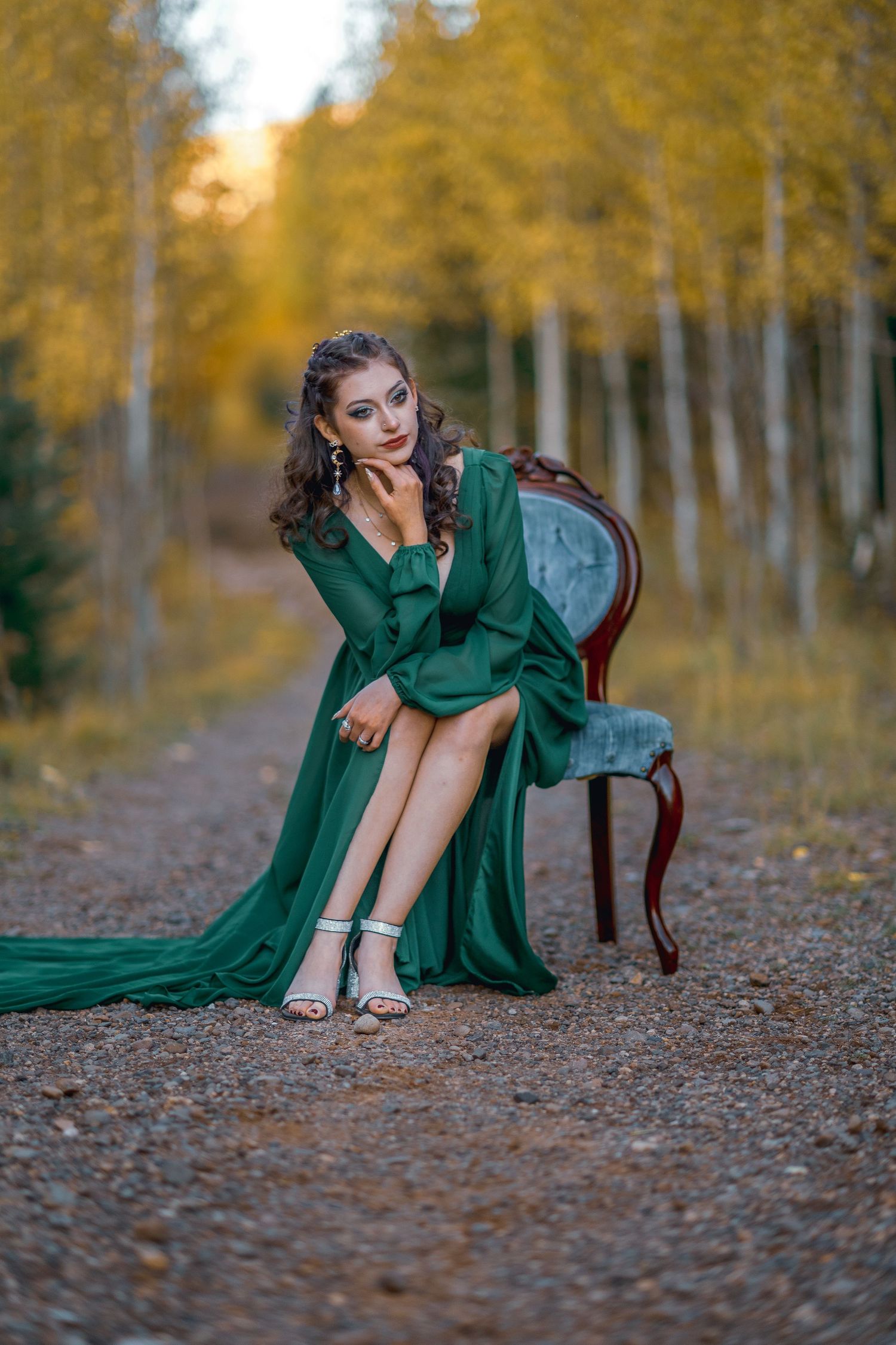 An emerald green dress flows gracefully among golden autumn aspen trees as someone poses on fallen leaves.