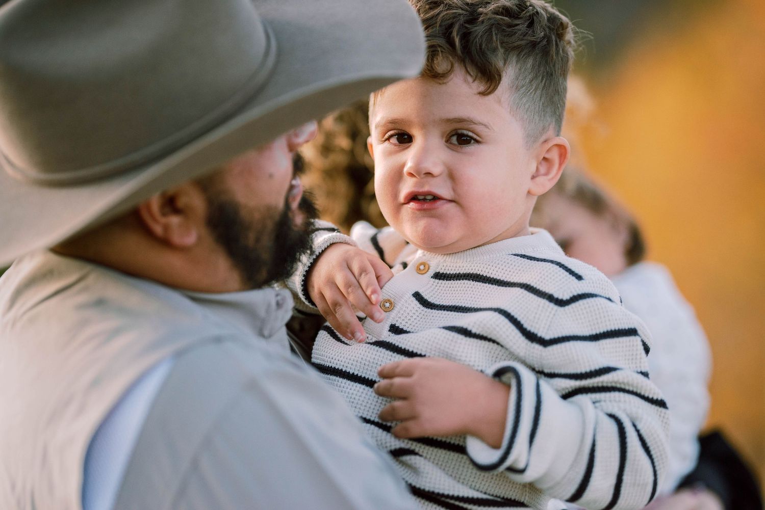 A tender moment captured between a father in a hat and a child wearing a striped shirt.