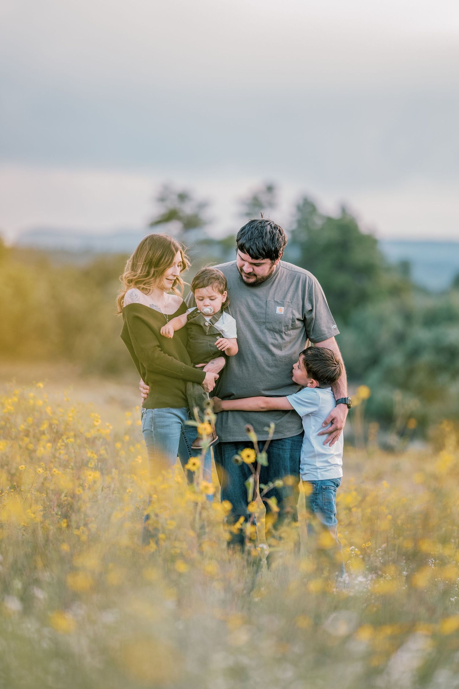 Family of three sharing joyful interactions in a field of yellow wildflowers.