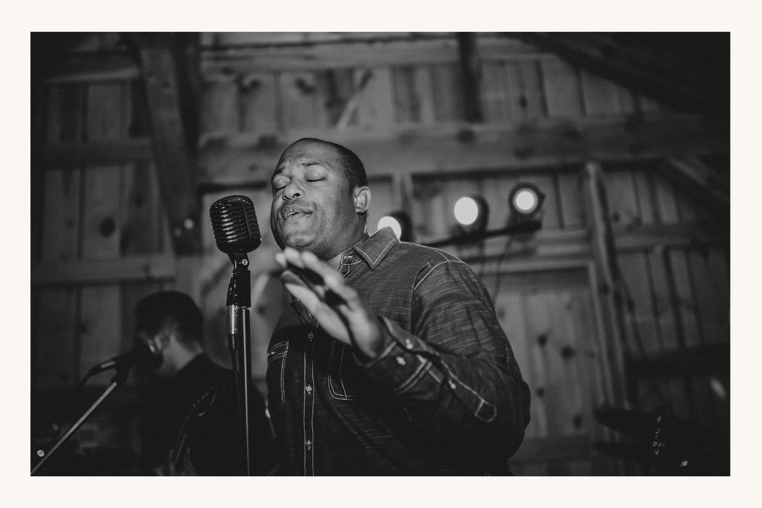 Black and white photo of a male singer performing at a vintage microphone on stage under warm lights.