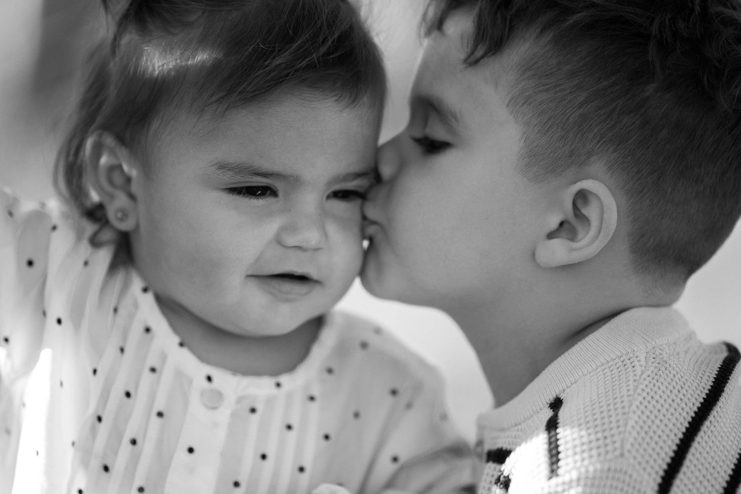A black and white photo captures a tender moment between two children smiling and interacting together.