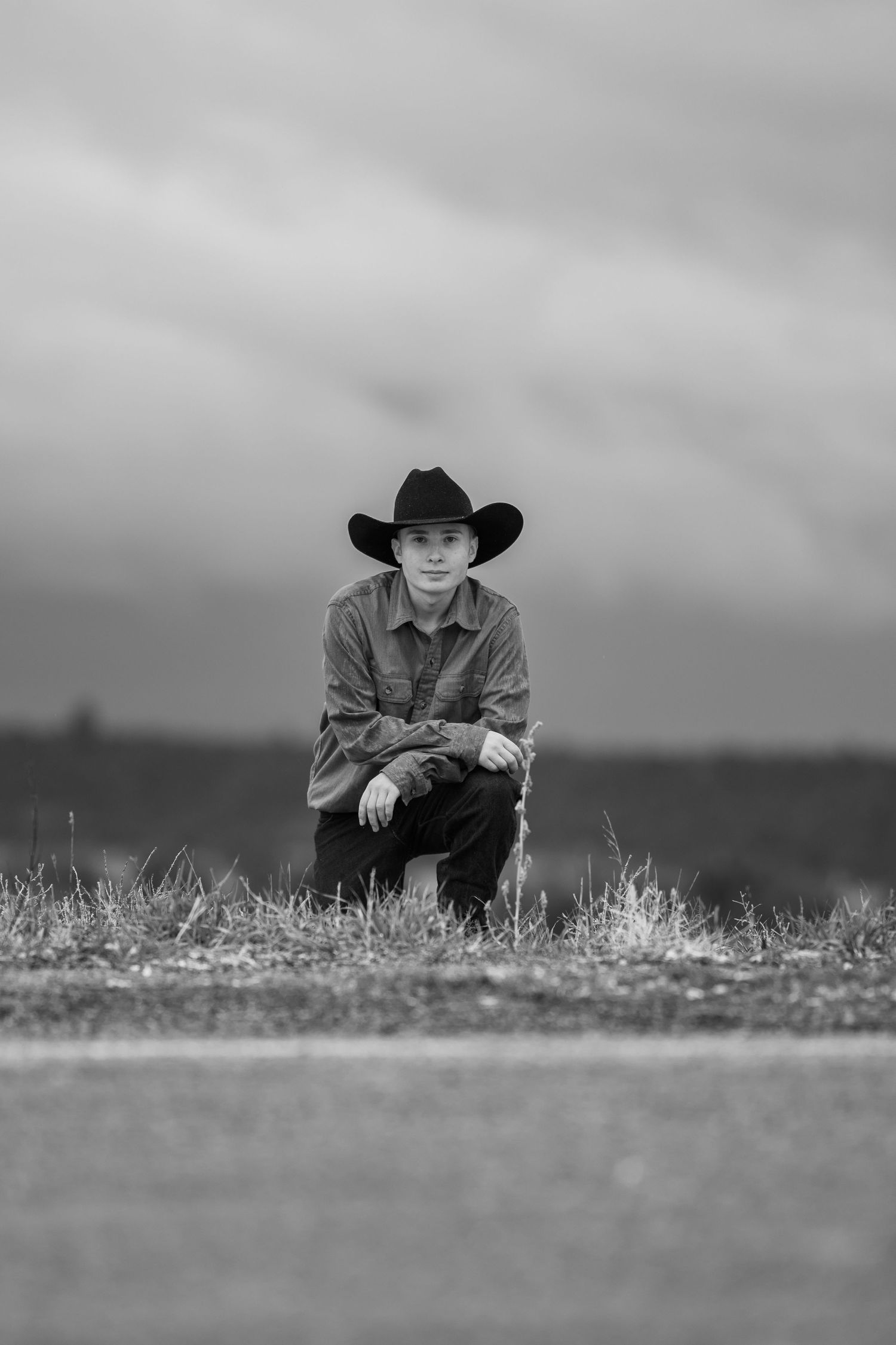 A black and white western-style portrait series shows someone wearing a cowboy hat resting near the ground in a field.