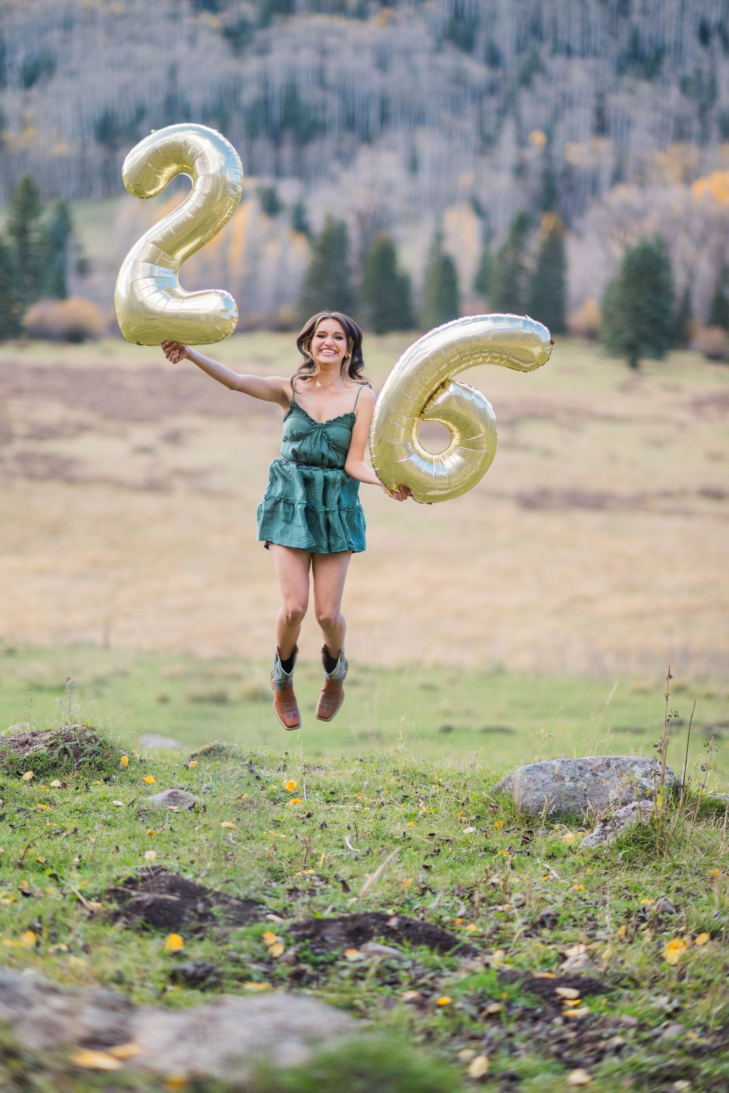A series of action shots shows someone jumping in a green dress while holding large gold number balloons in a mountain field.