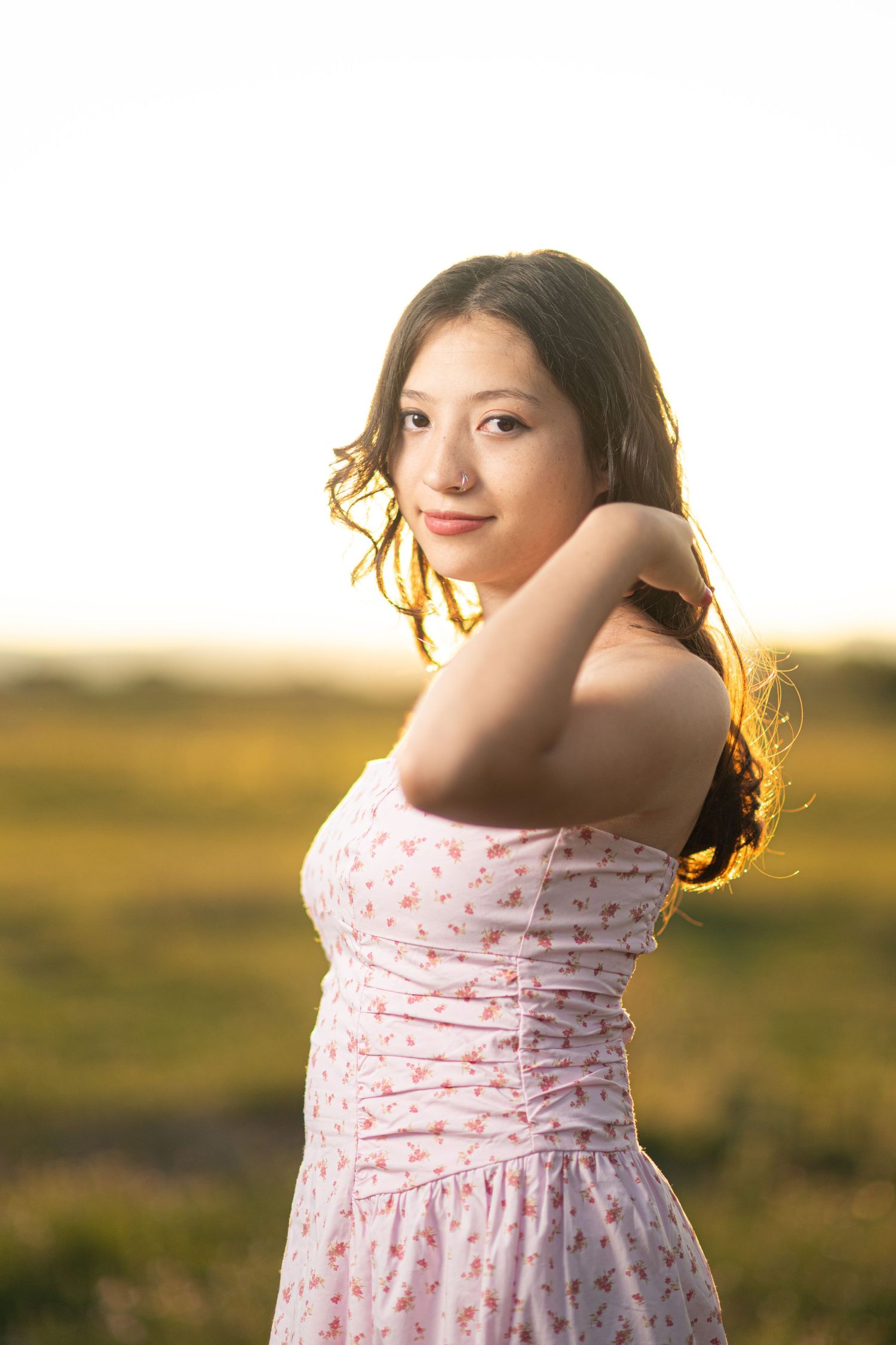 A person in a pink polka dot dress poses playfully against a golden sunset backdrop in a grassy field.