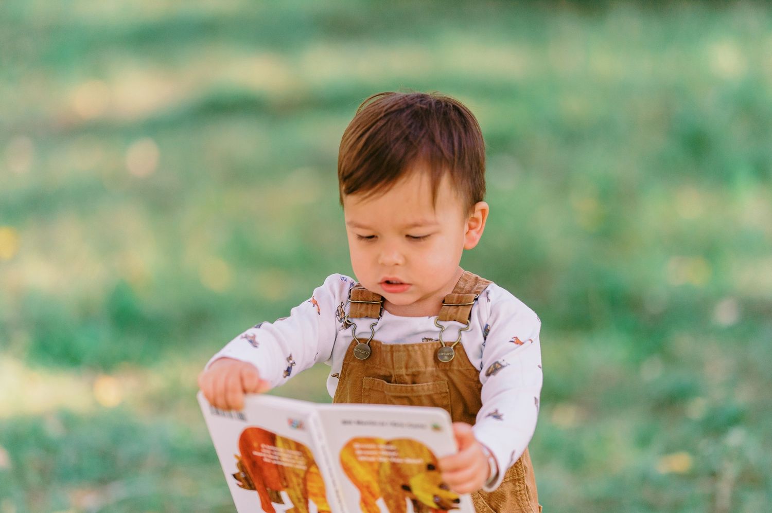 A young child in a white shirt sits on grass while playing with a wooden toy during a sunny day outdoors.