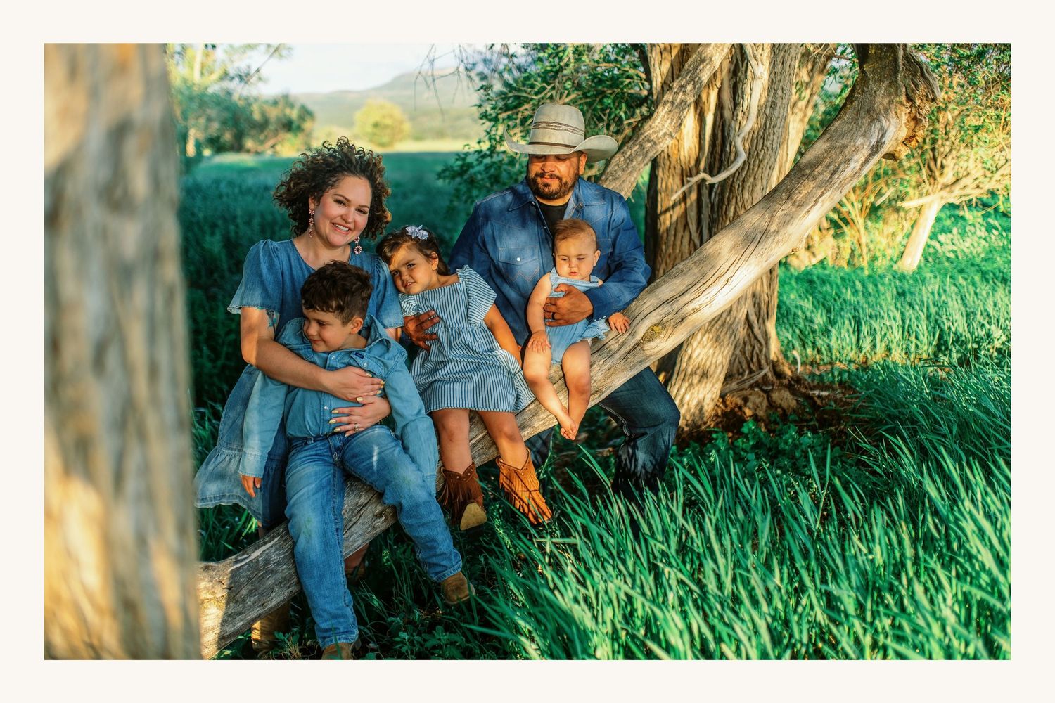 Happy family of five sitting on a wooden bench under a tree in a lush green field on a sunny day.
