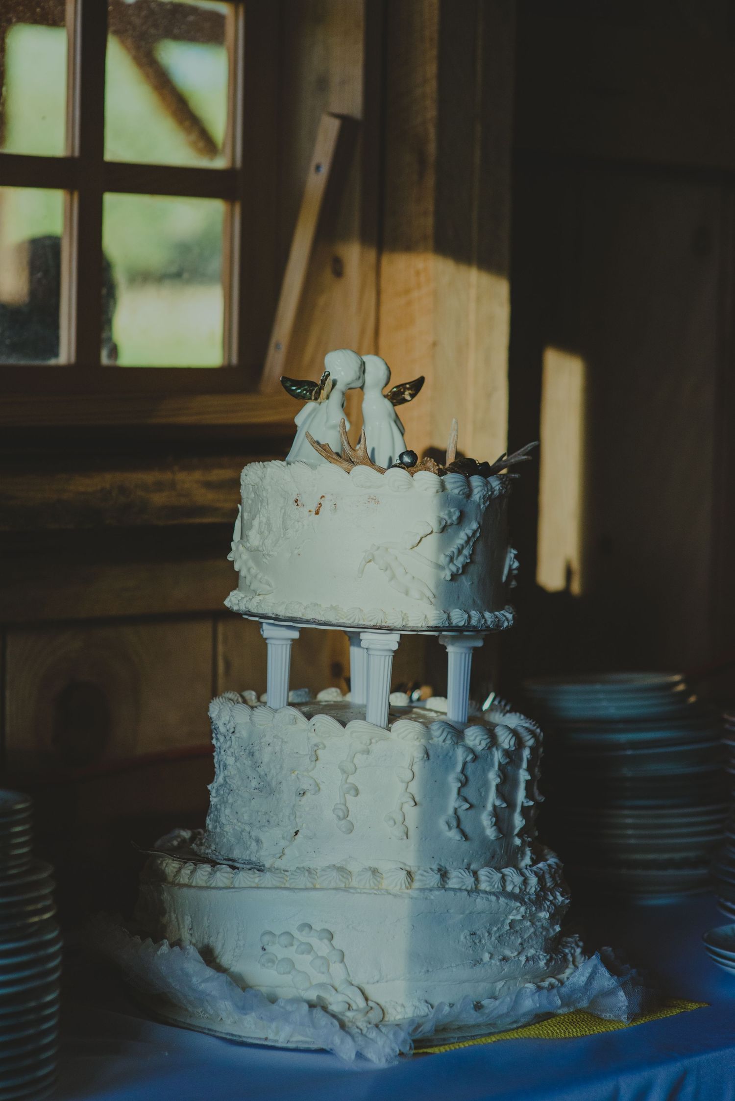 Three-tiered white wedding cake with delicate piping and a simple topper displayed near a window.