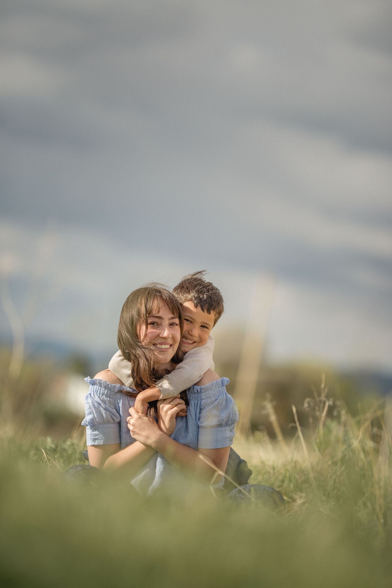 People embracing and laughing together while sitting in a grassy meadow on a cloudy afternoon.
