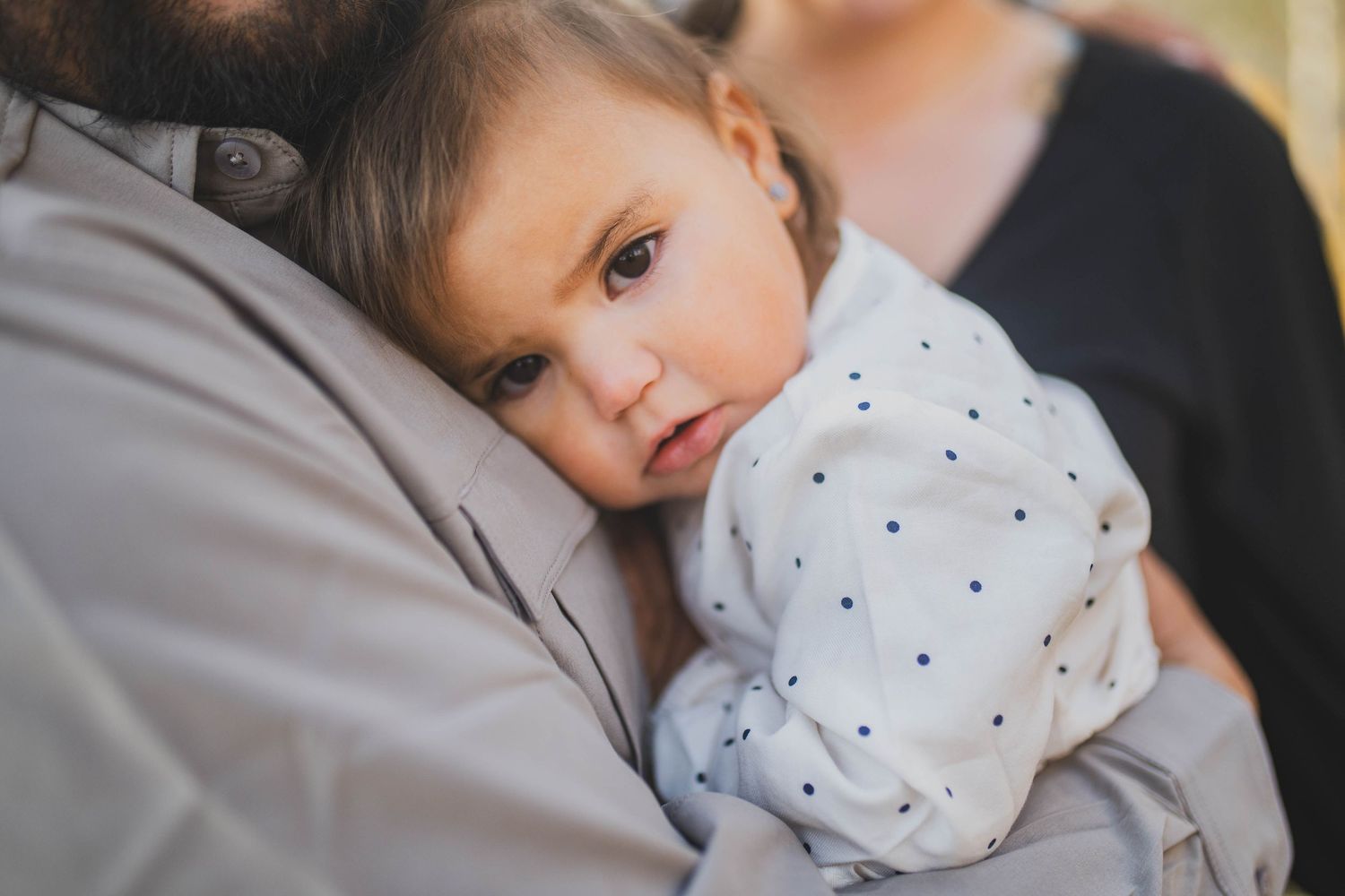 Family cuddles together on gray couch during tender indoor moment with infant.