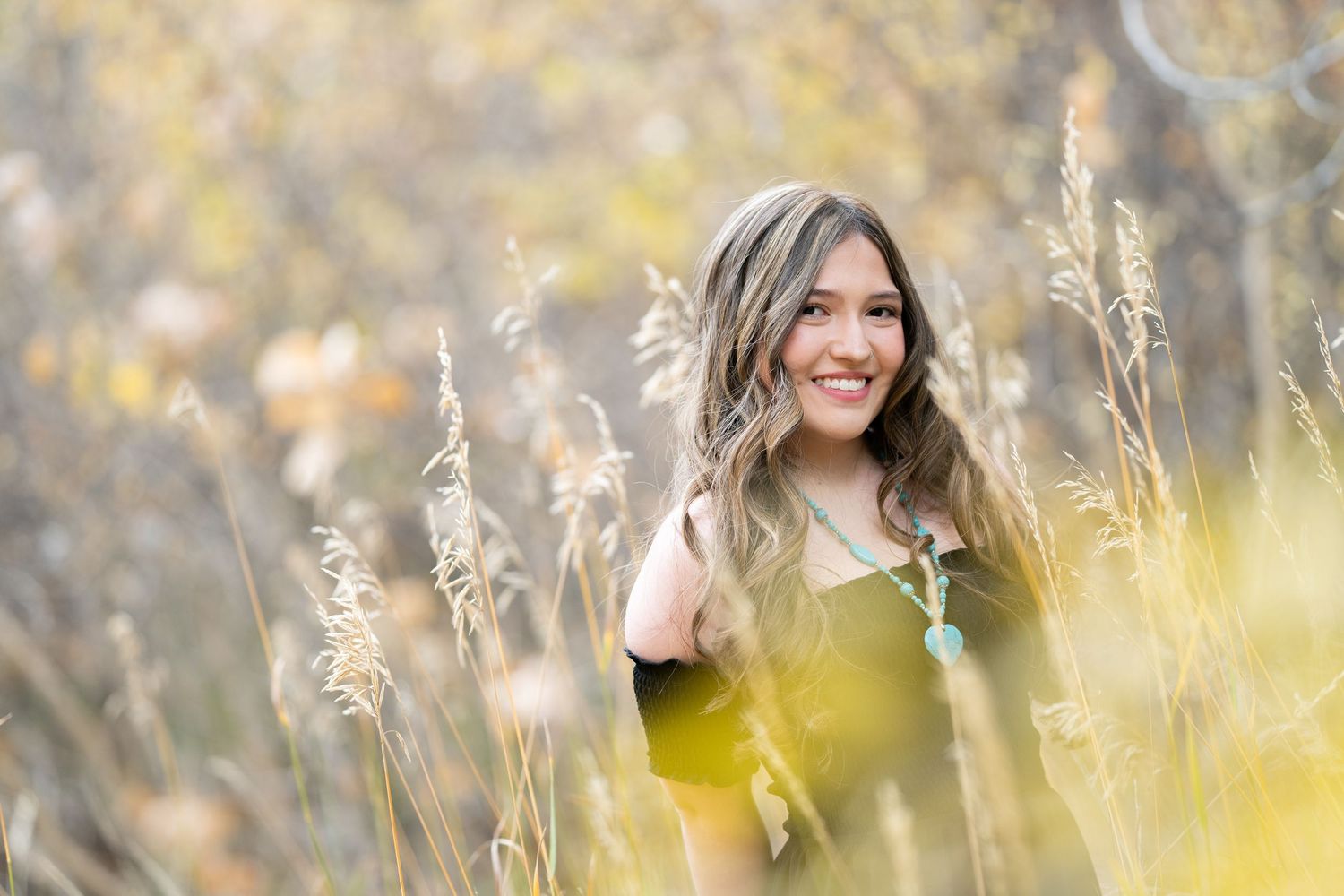 Young woman wearing yellow sweater poses in golden autumn field with tall grass and natural sunlight.