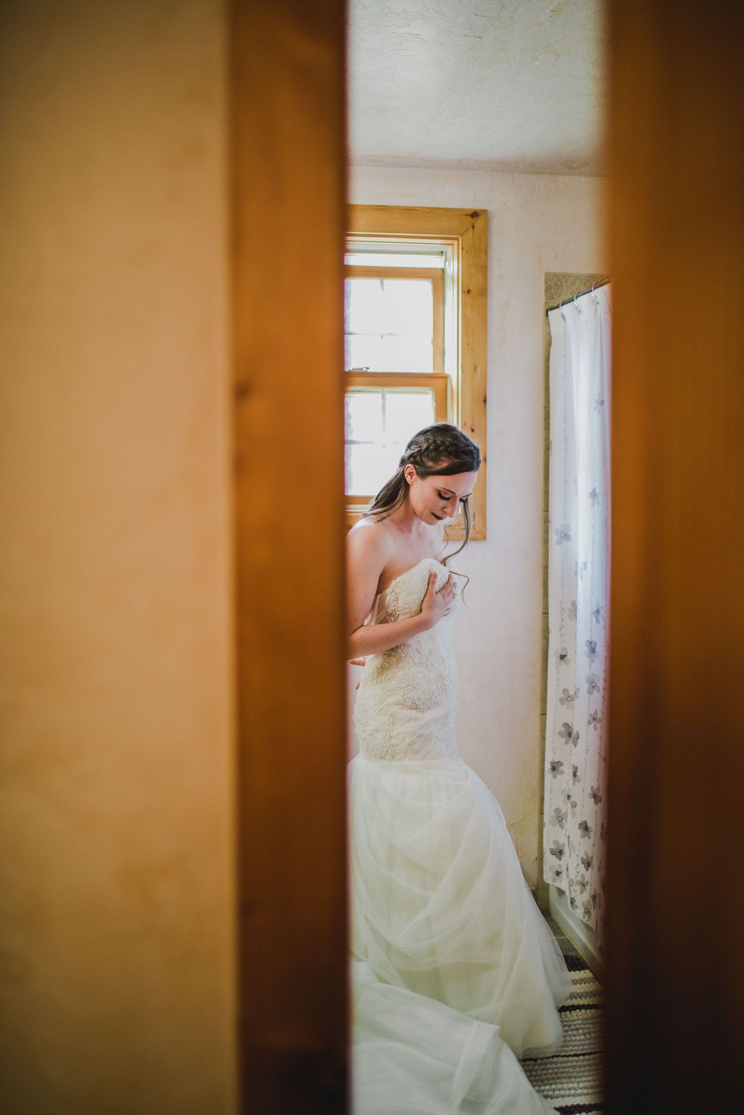 Artistic wedding photo showing a glimpse of a bride in white dress through a doorway.