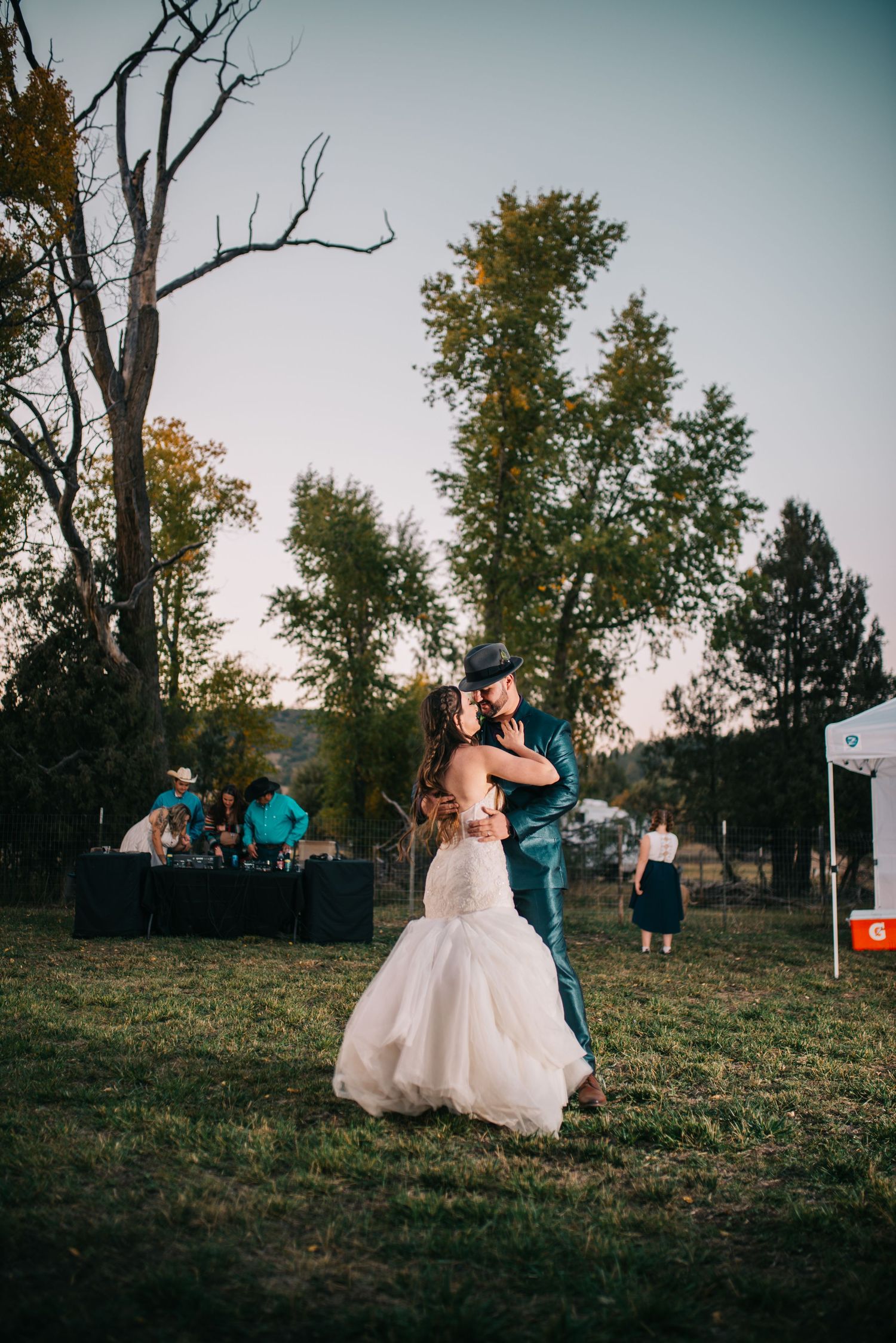 Outdoor wedding reception dance under evening sky with band performing in background.