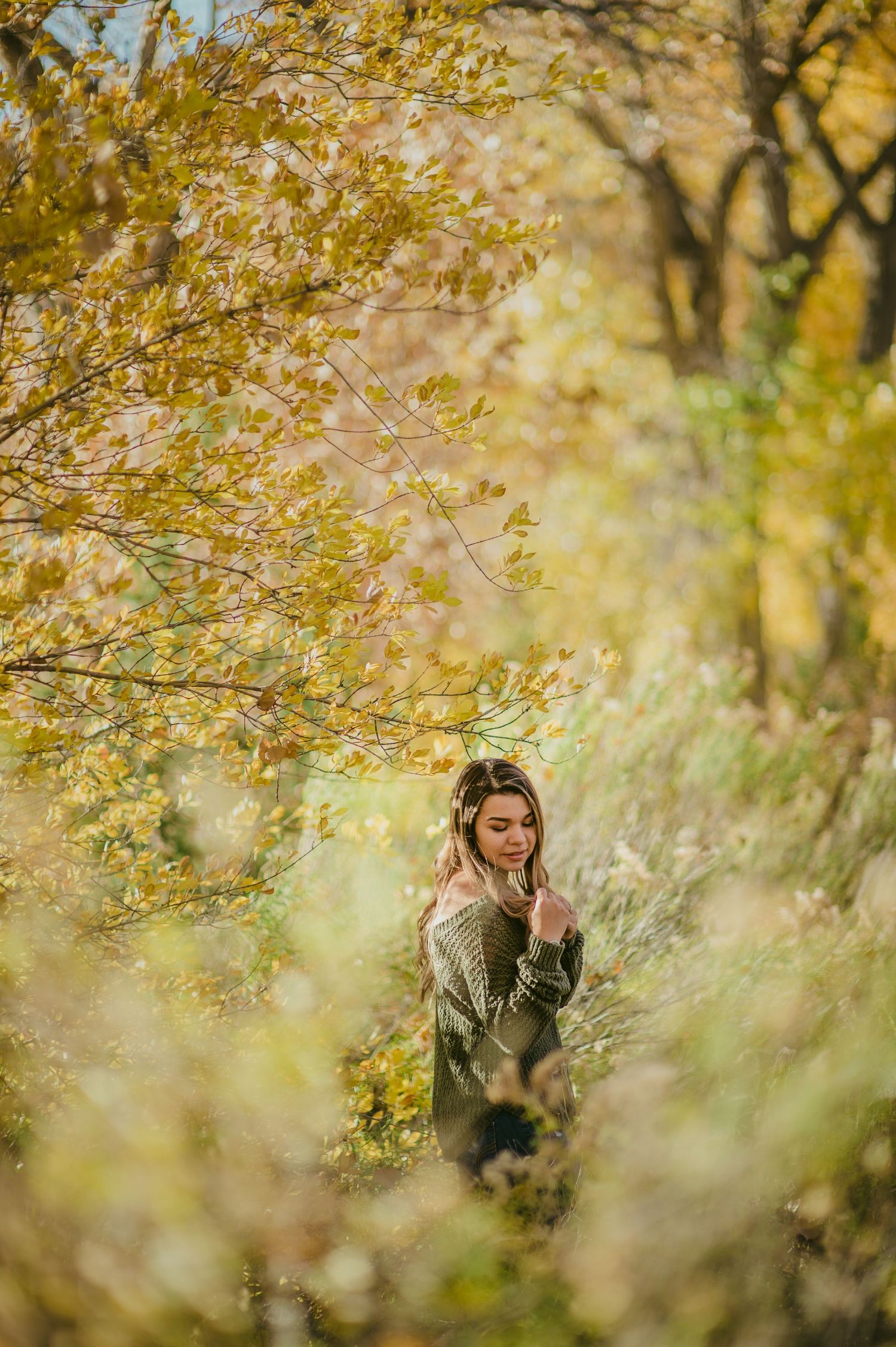 Artistic portrait framed by golden autumn foliage with dreamy bokeh effect.