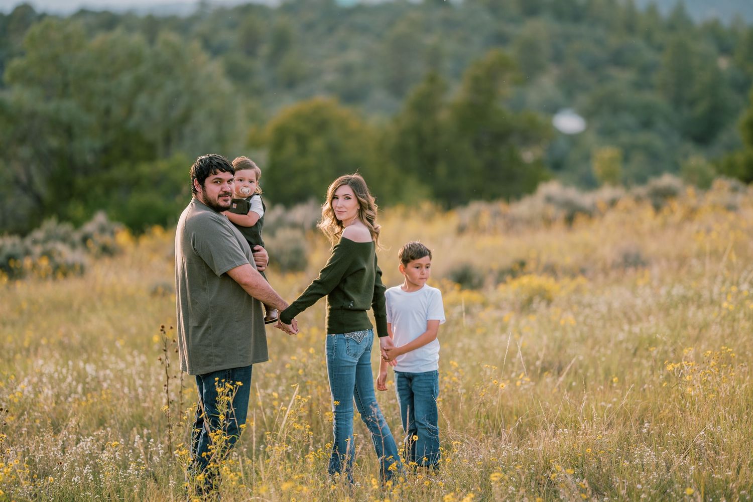 Parents and two children strolling in a sunlit meadow during early evening — warm family moment by The Amoras.