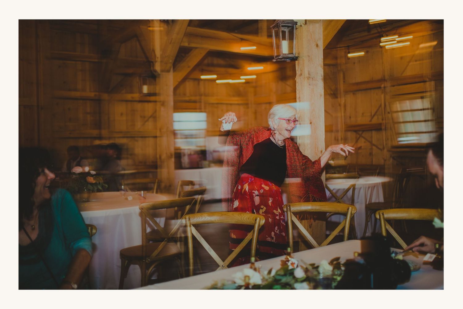 Elderly woman dancing joyfully in a rustic barn venue during a wedding reception celebration.
