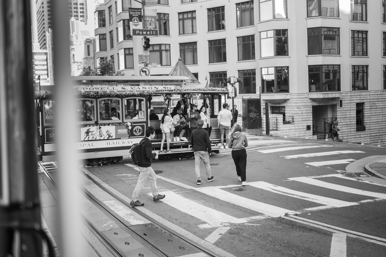 Black and white photograph of woman walking past railroad tracks in a busy urban street scene in San Francisco.