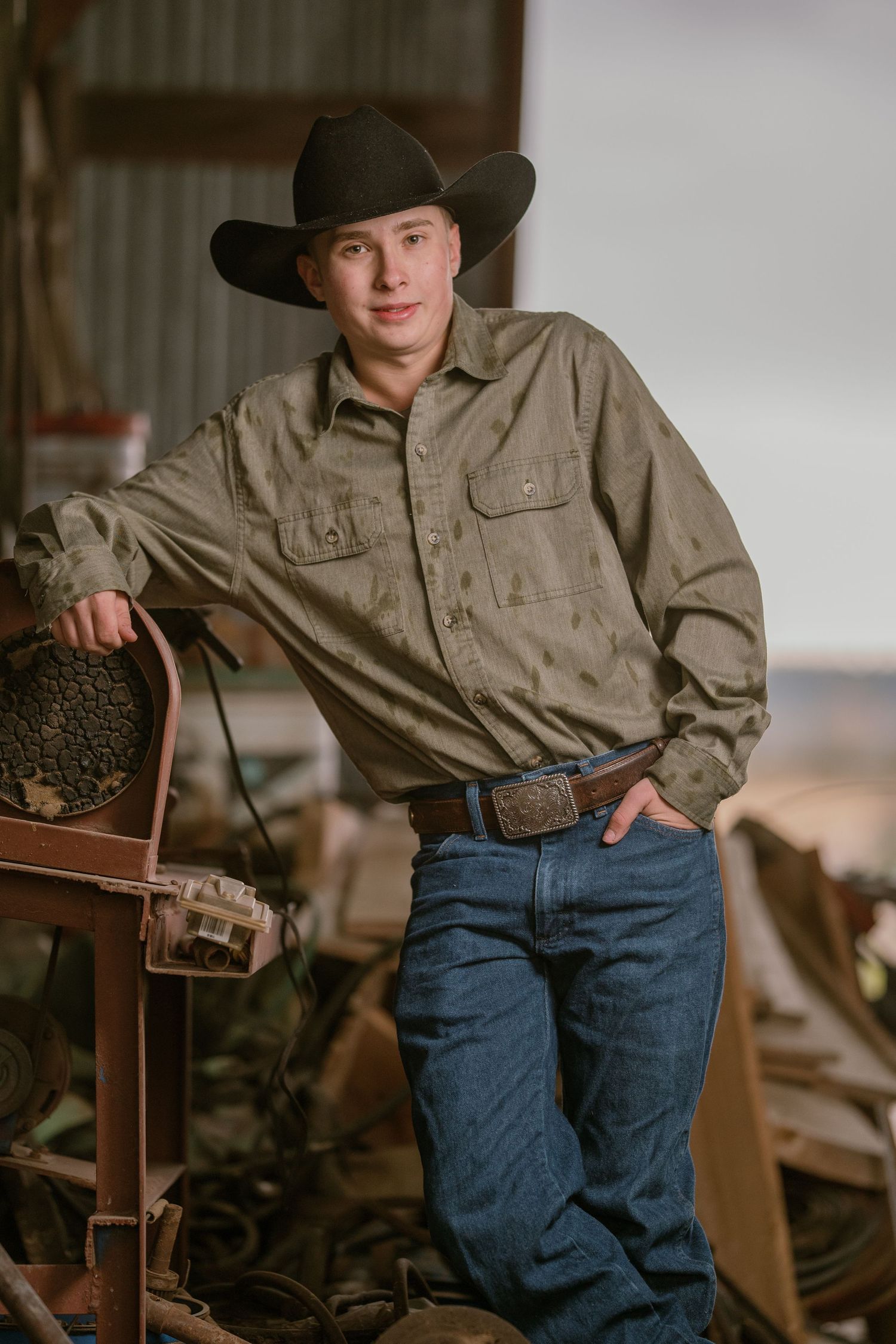 Someone in cowboy attire with brown jacket and blue jeans sits in vintage Western setting with rustic decor.