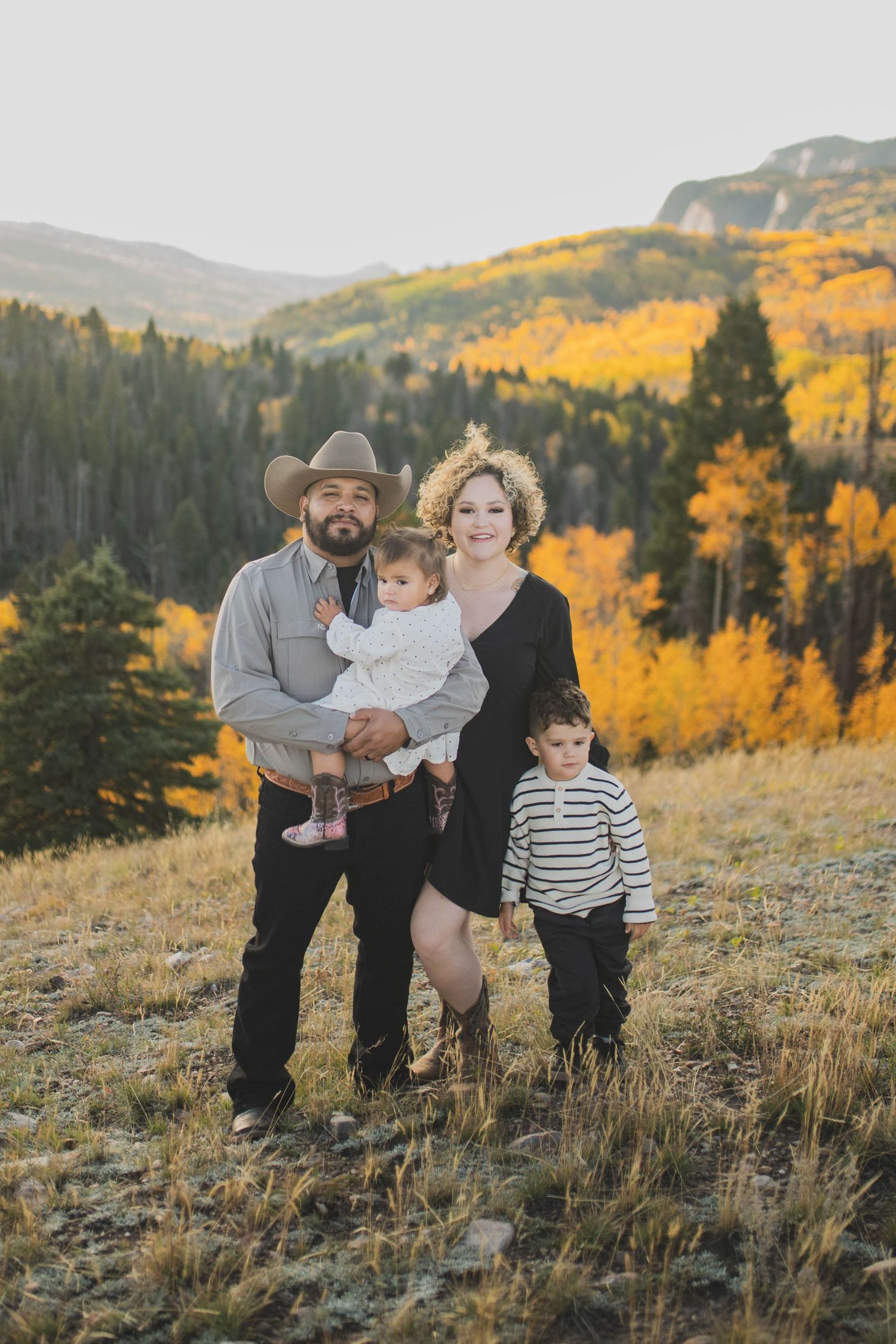 A family poses together on a mountainside during autumn with golden aspen trees visible in the background.
