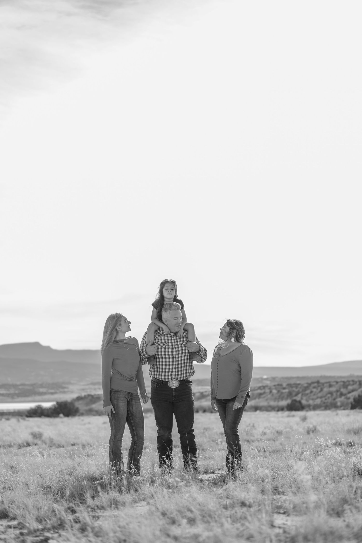 A black and white photograph of a family standing together in a desert landscape with mountains in the background.