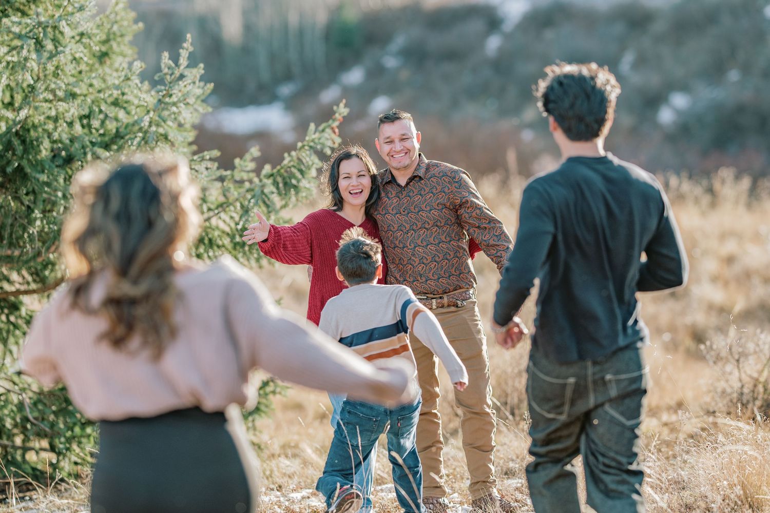 Group of people playfully interacting in a sunlit field with natural scenery in the background during golden hour.